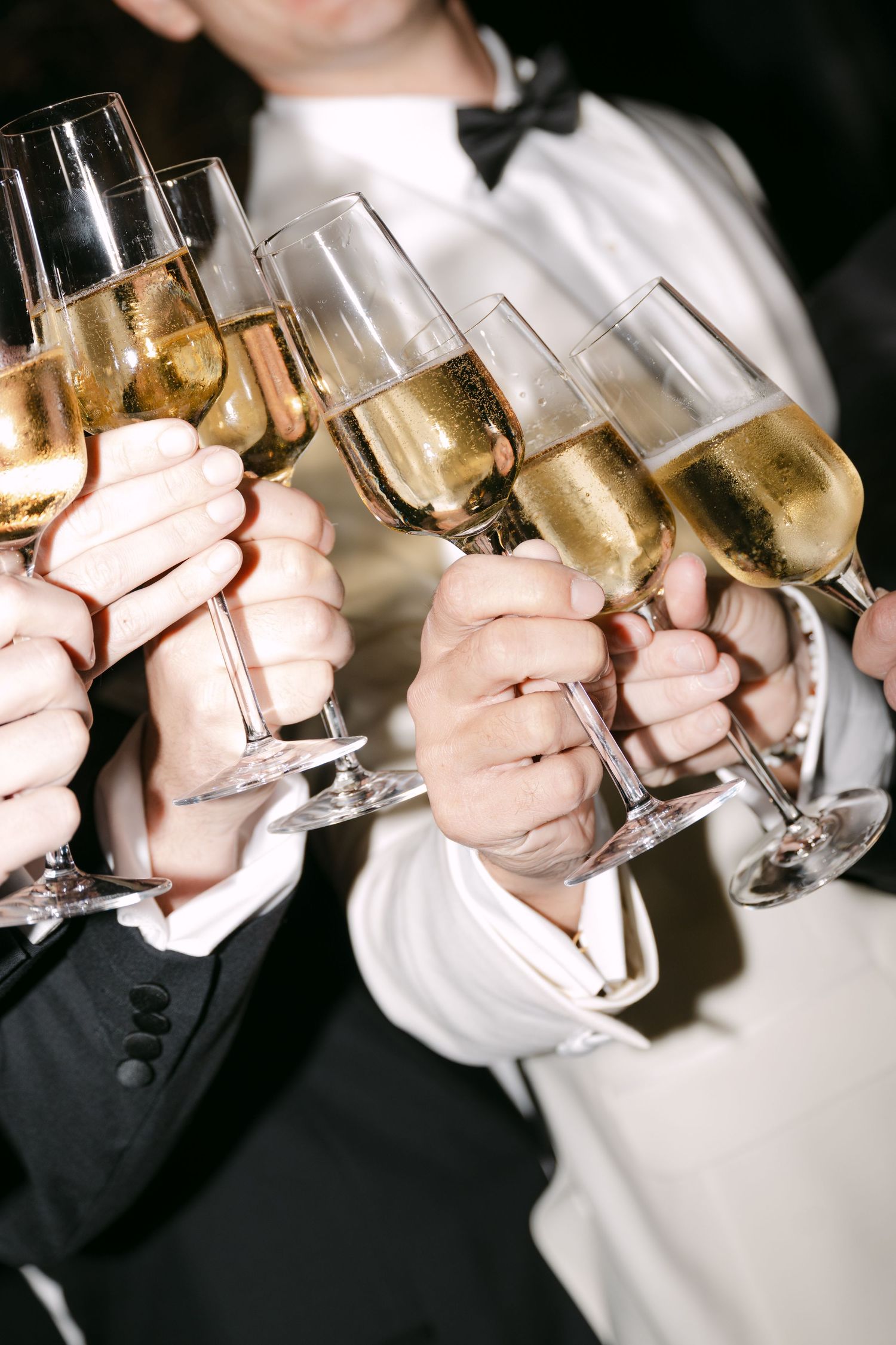 Close-up of wedding party clinking champagne flutes in a celebratory toast at formal event.