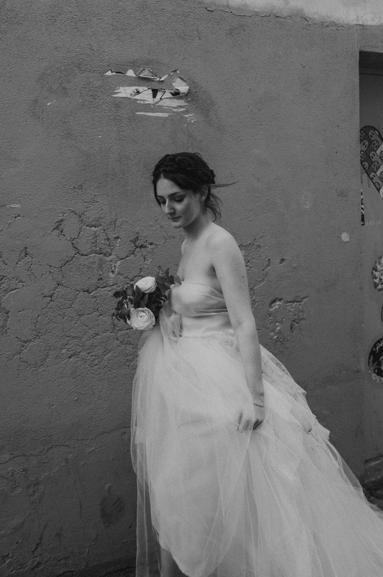 Black and white portrait showcasing a delicate strapless wedding gown against textured wall.