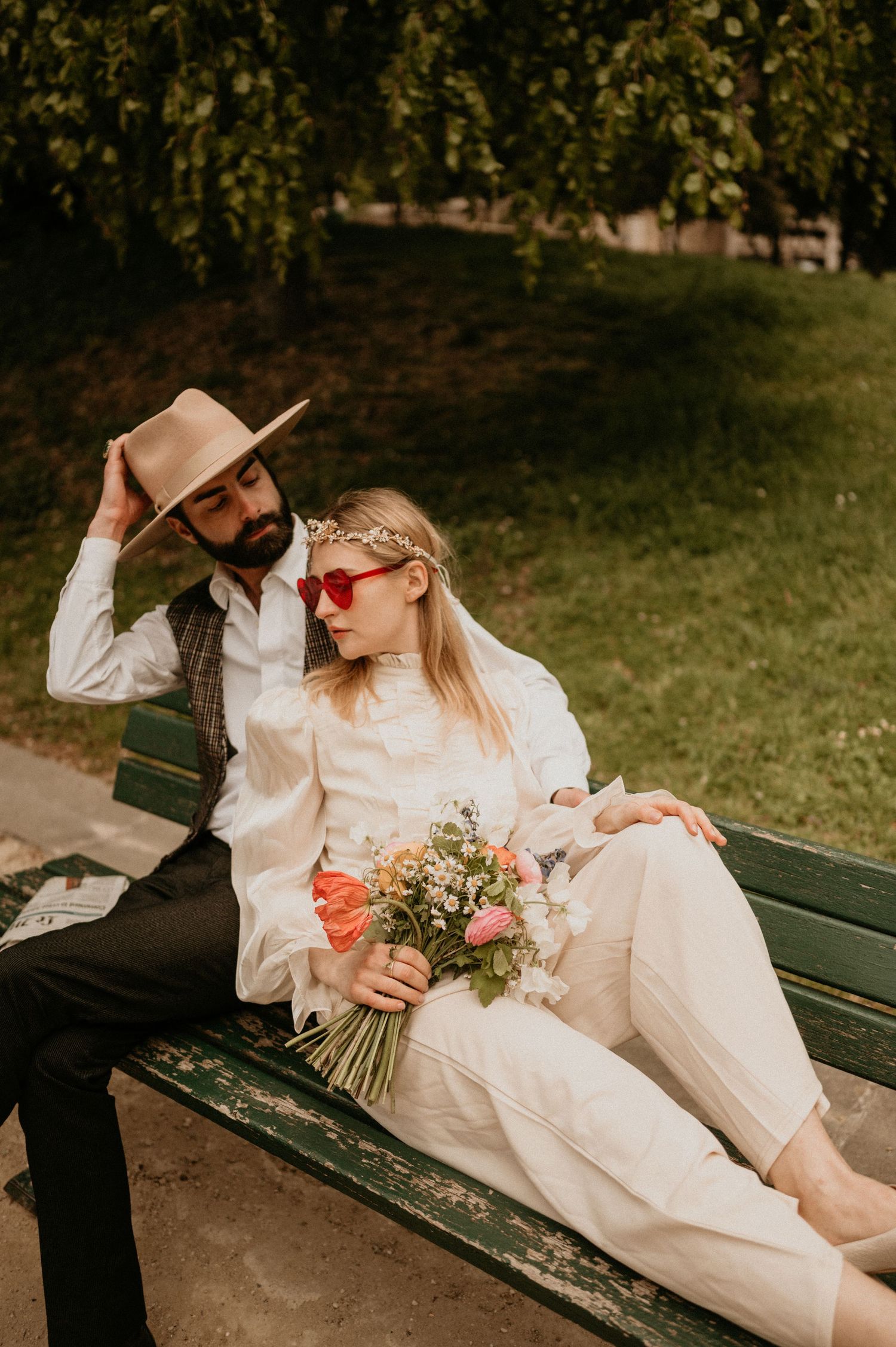 Stylish couple on park bench with bouquet and hat in warm autumn setting.