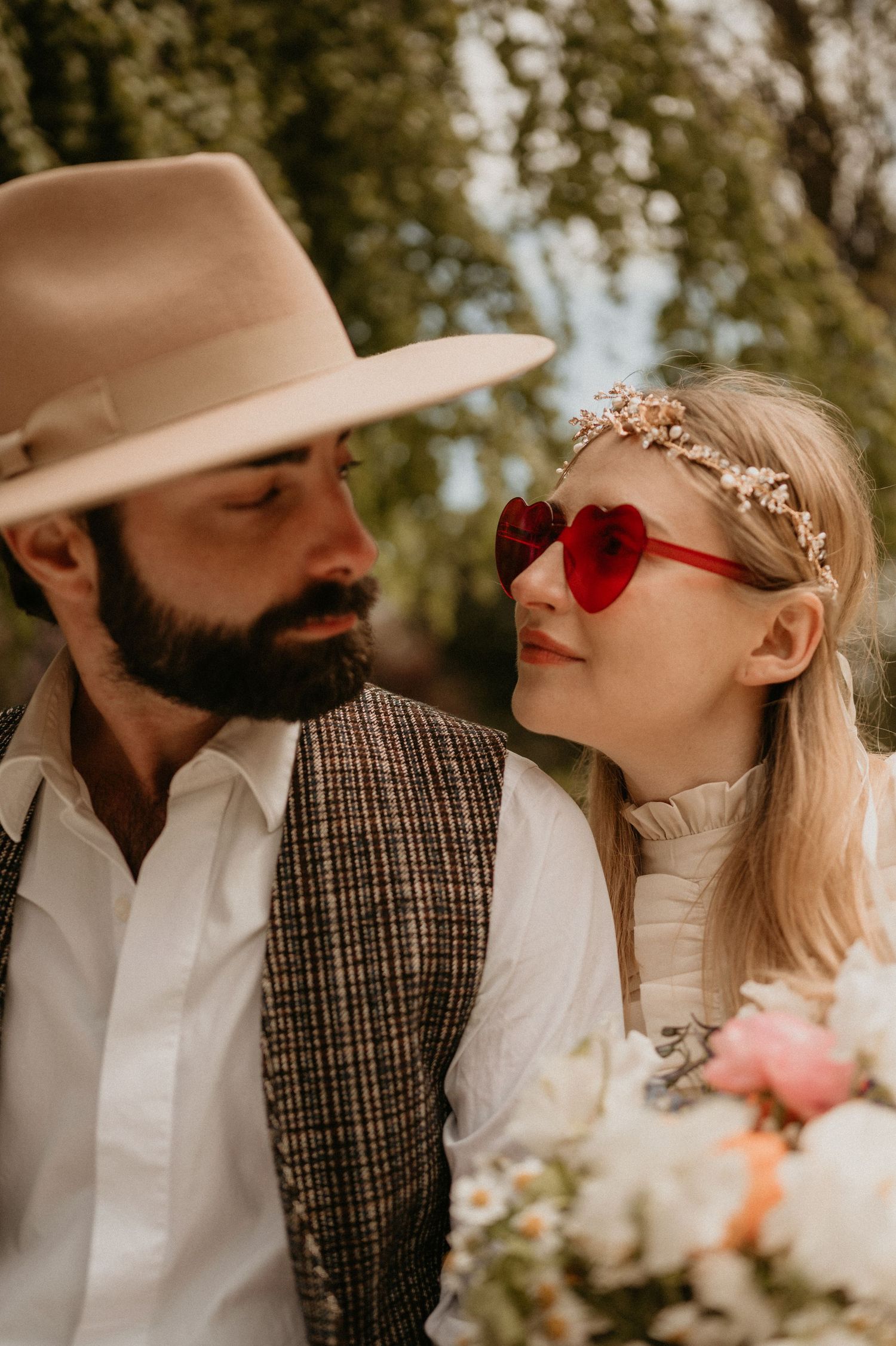 A tender moment captured between a couple wearing vintage-inspired clothing and red accessories in a park setting.