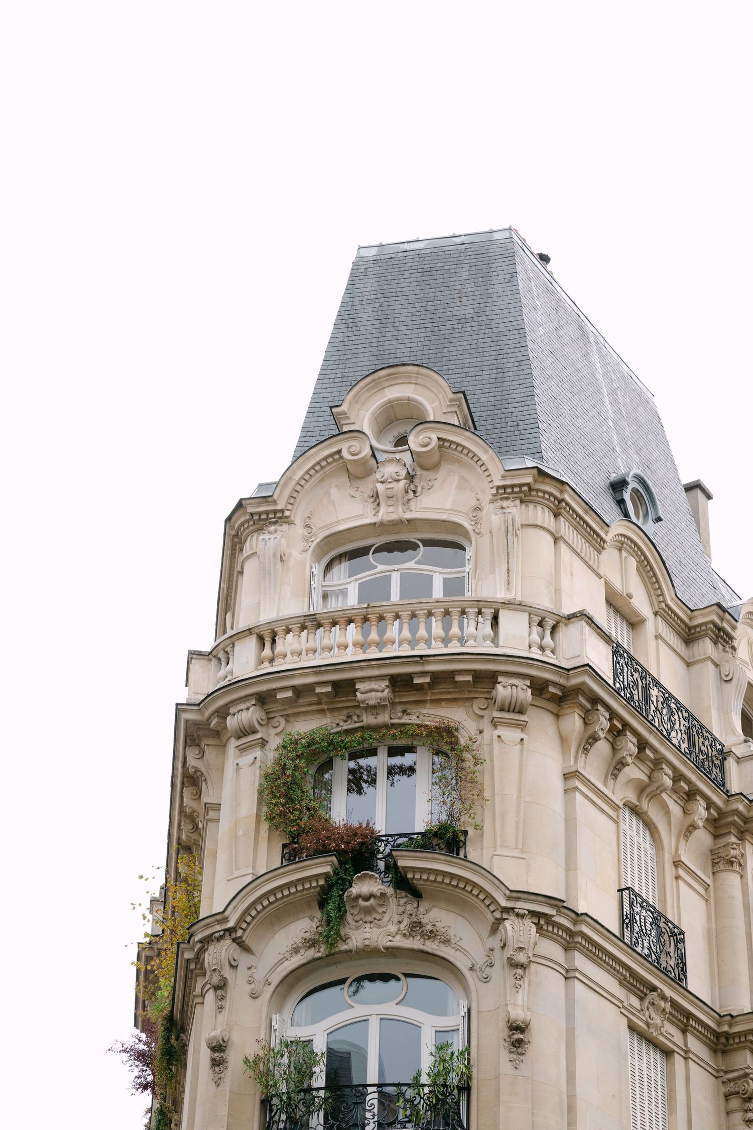Ornate beige Parisian apartment building with elegant architectural details and wrought iron balconies against a cloudy sky.