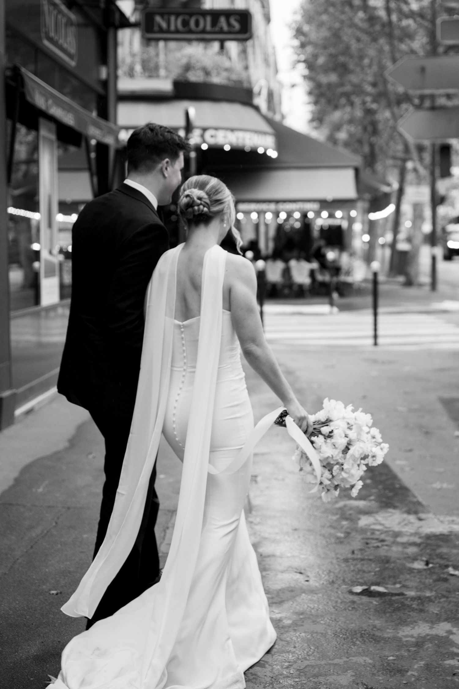 A black and white wedding photo series showing a couple walking together on a city street with a white dress flowing.