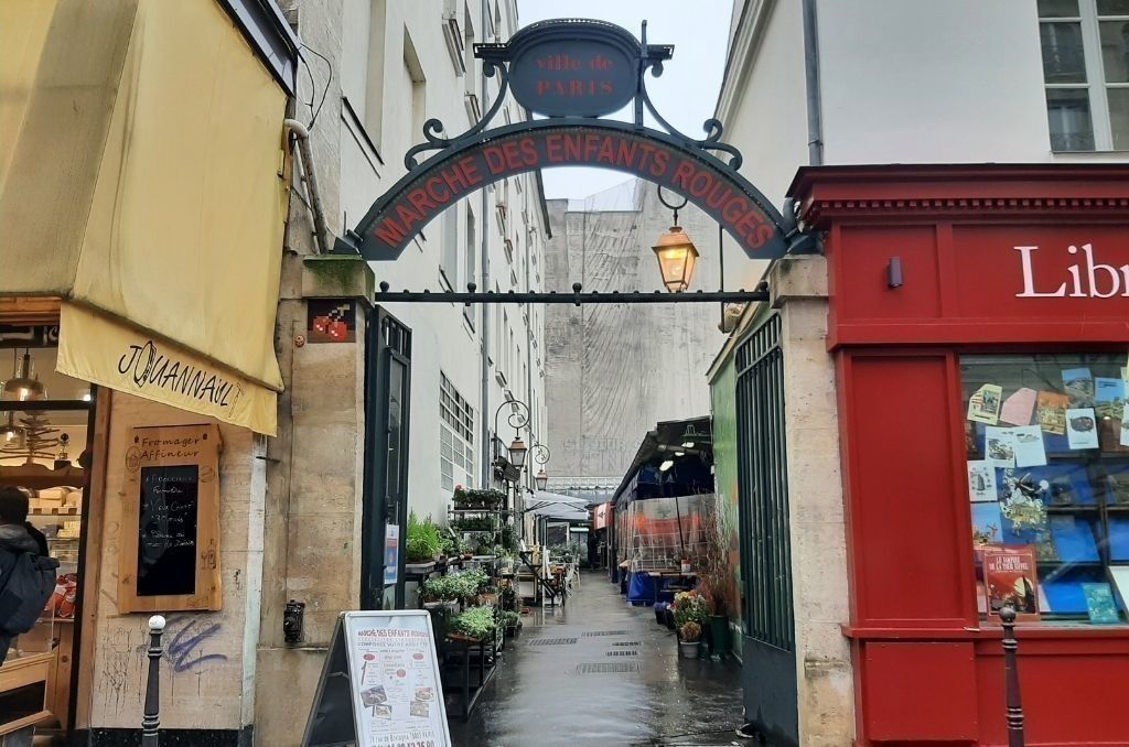 A narrow Parisian passage with traditional storefronts and an ornate archway overhead.