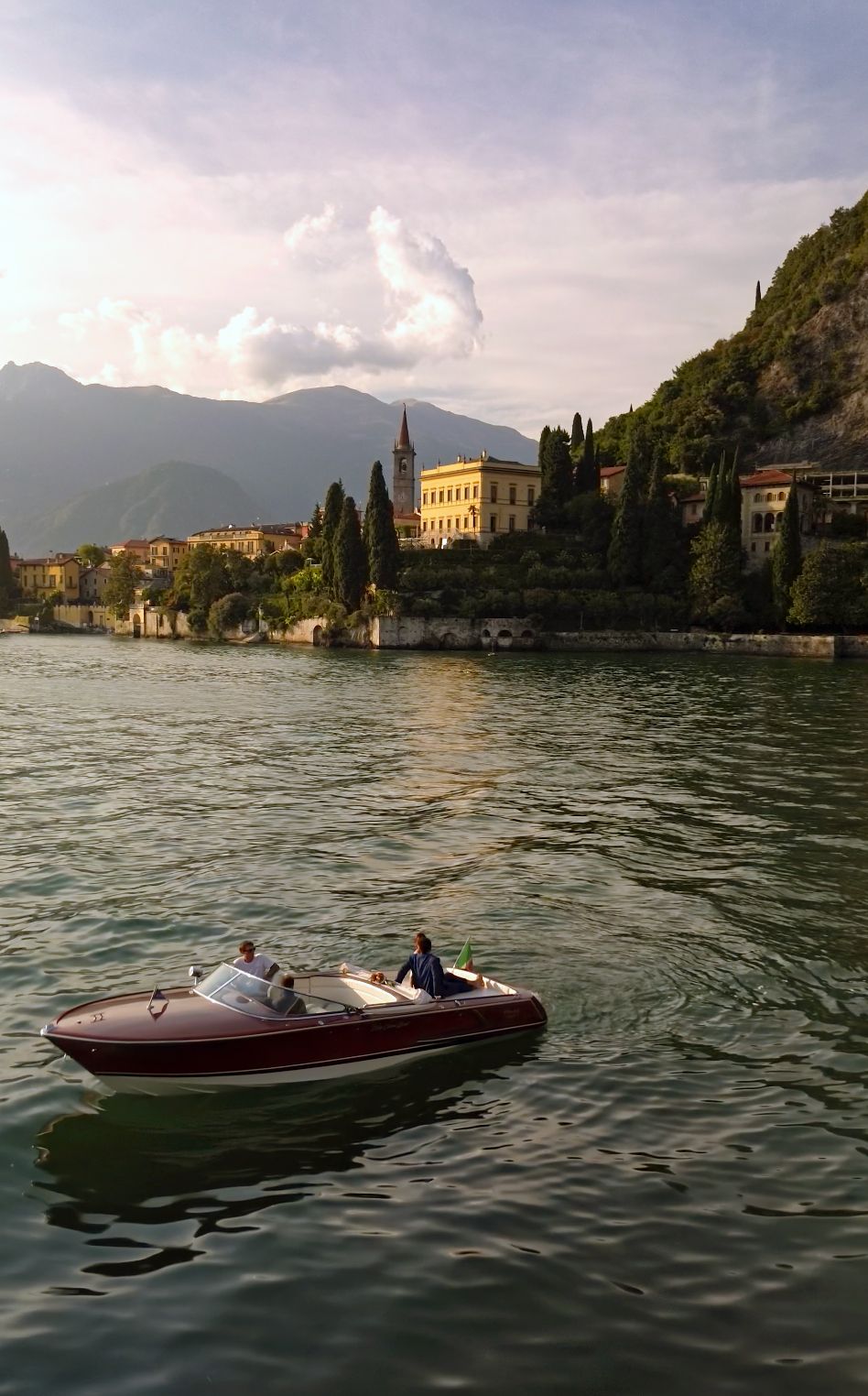 A classic red speedboat glides across Lake Como with a grand villa and lush hills in the background.