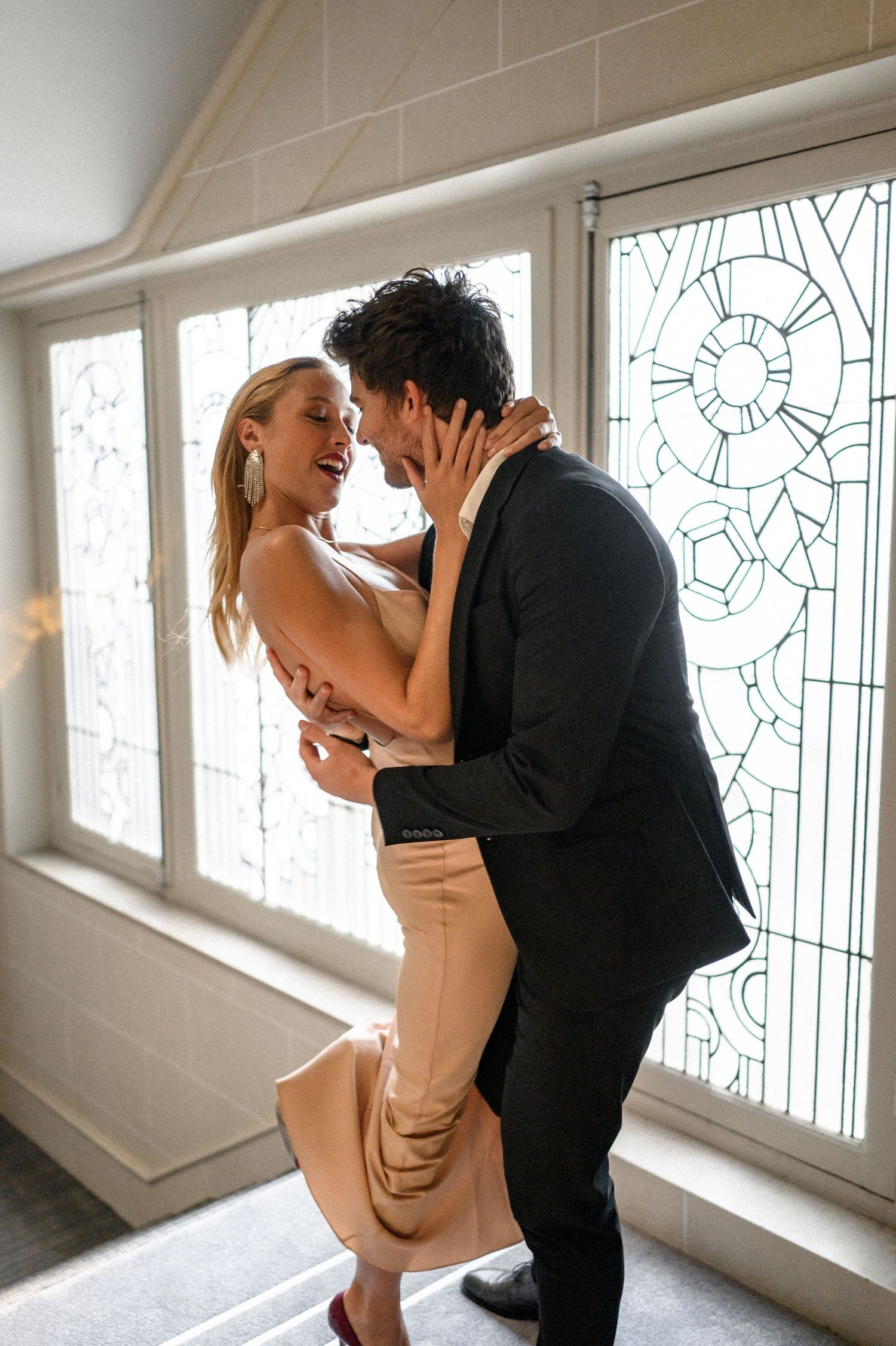 Romantic couple in formal attire sharing an intimate moment near ornate stained glass windows.