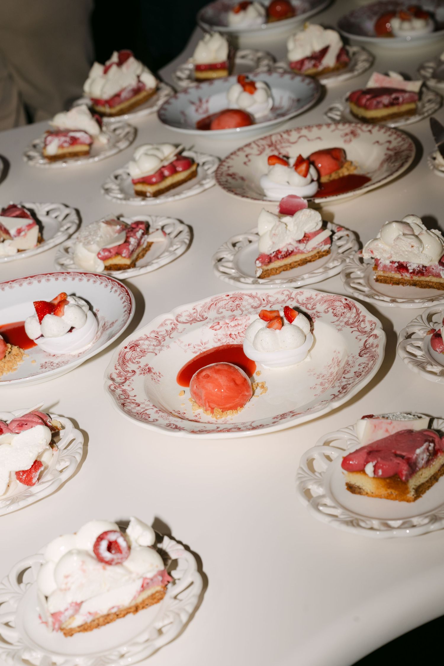 Elegant dessert display of strawberry tarts and cream on ornate red and white patterned plates.