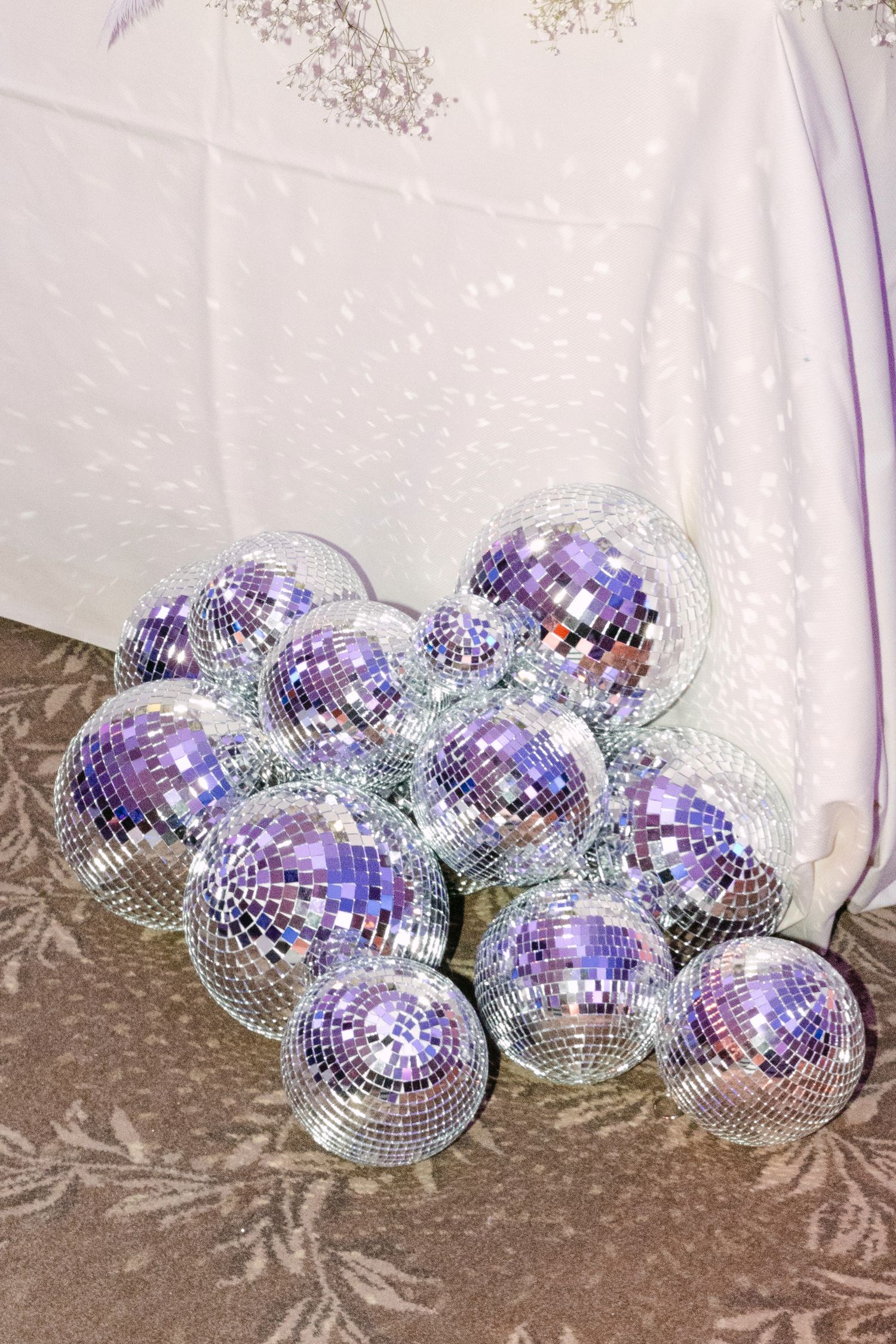 Collection of silver mirrored disco balls of various sizes arranged on the floor at a wedding venue.