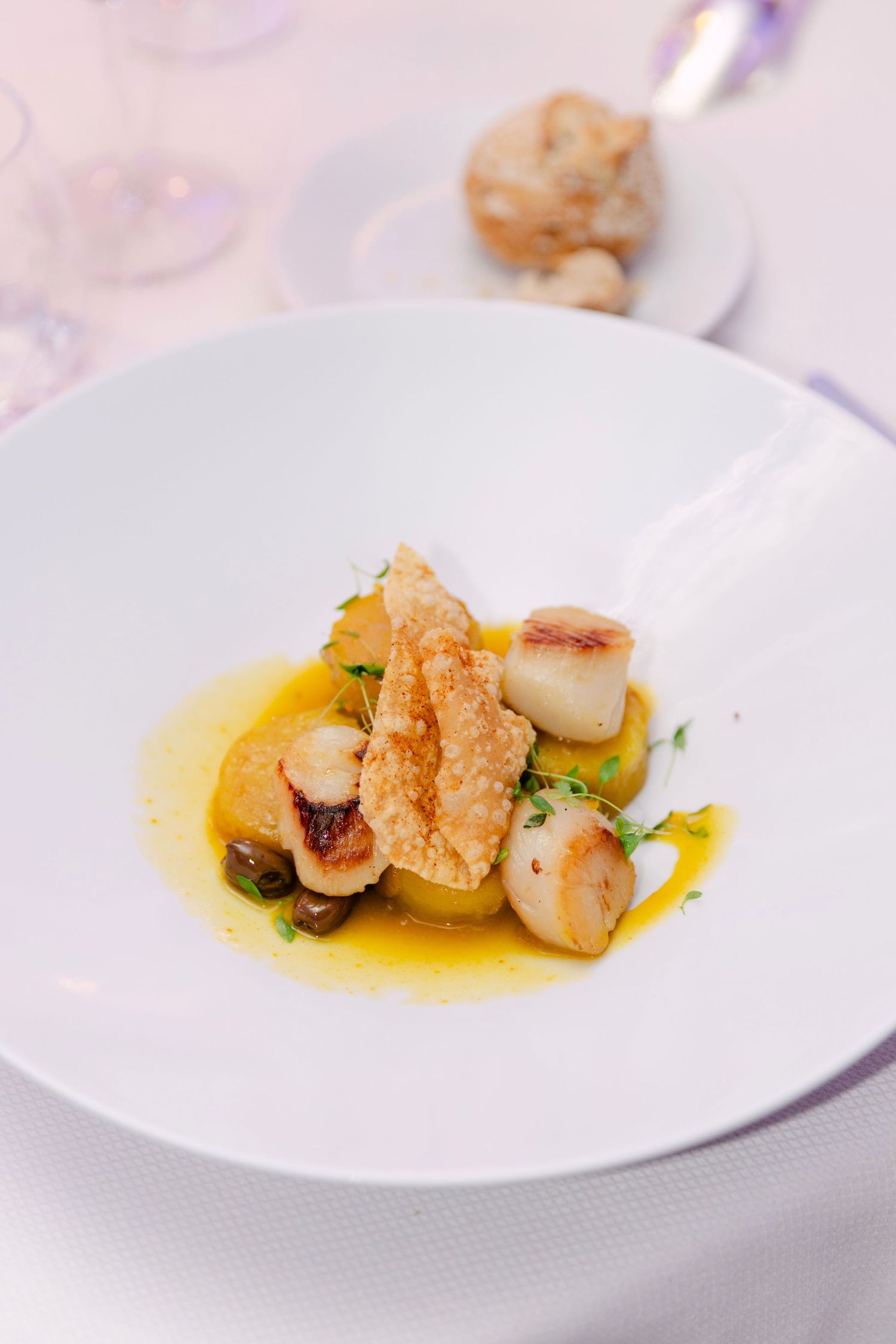 Elegantly plated seared scallops with golden sauce and crispy garnish served in a white bowl at a wedding dinner.