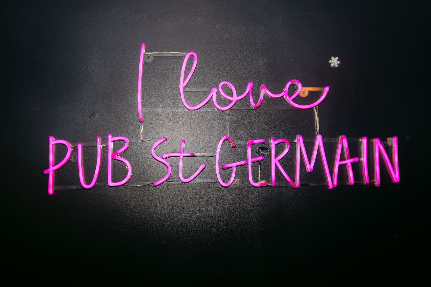 Pink neon sign reading I Love Pub St Germain on dark wall.