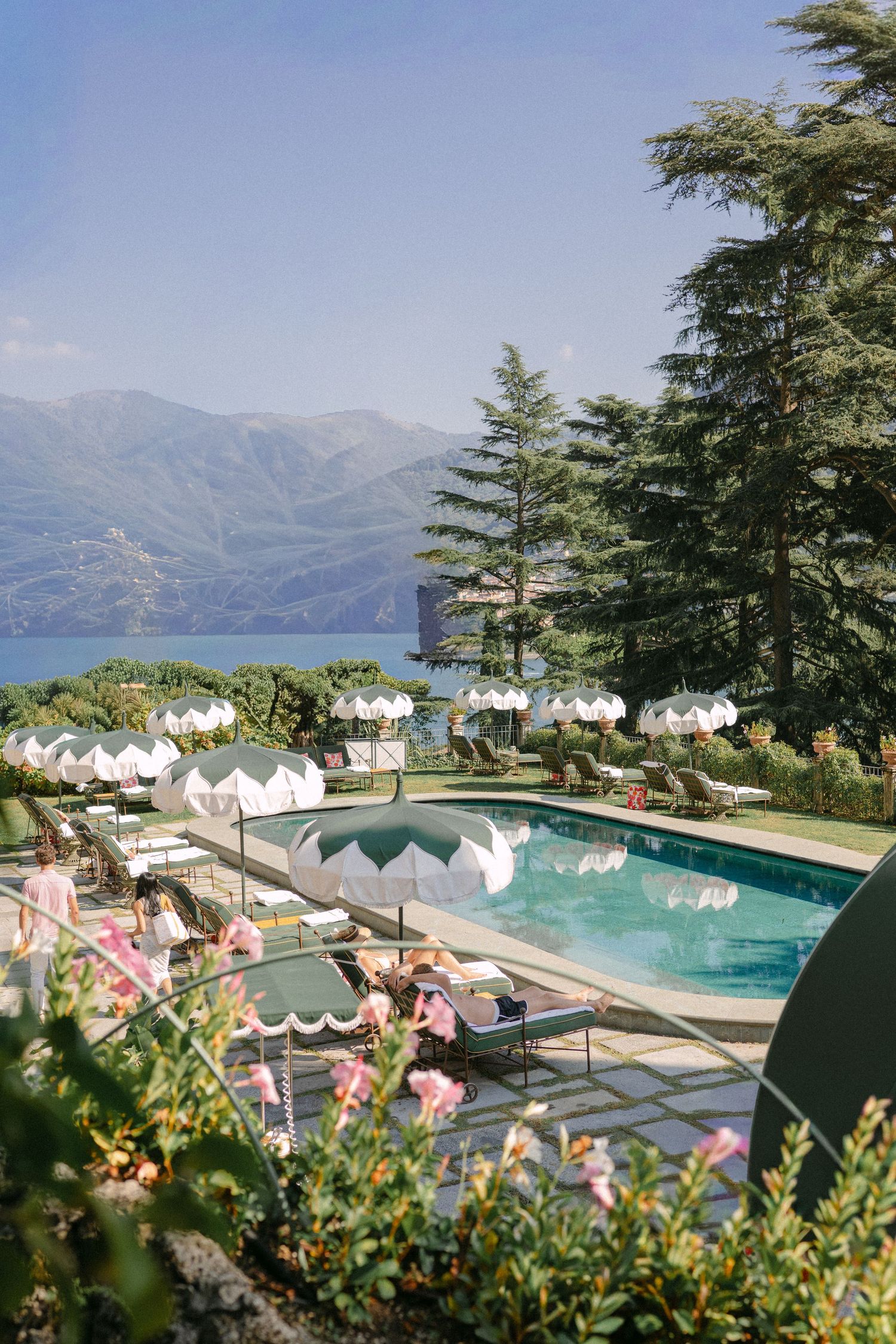 Elegant pool area with white umbrellas and lounge chairs overlooking a serene lake and mountain landscape.