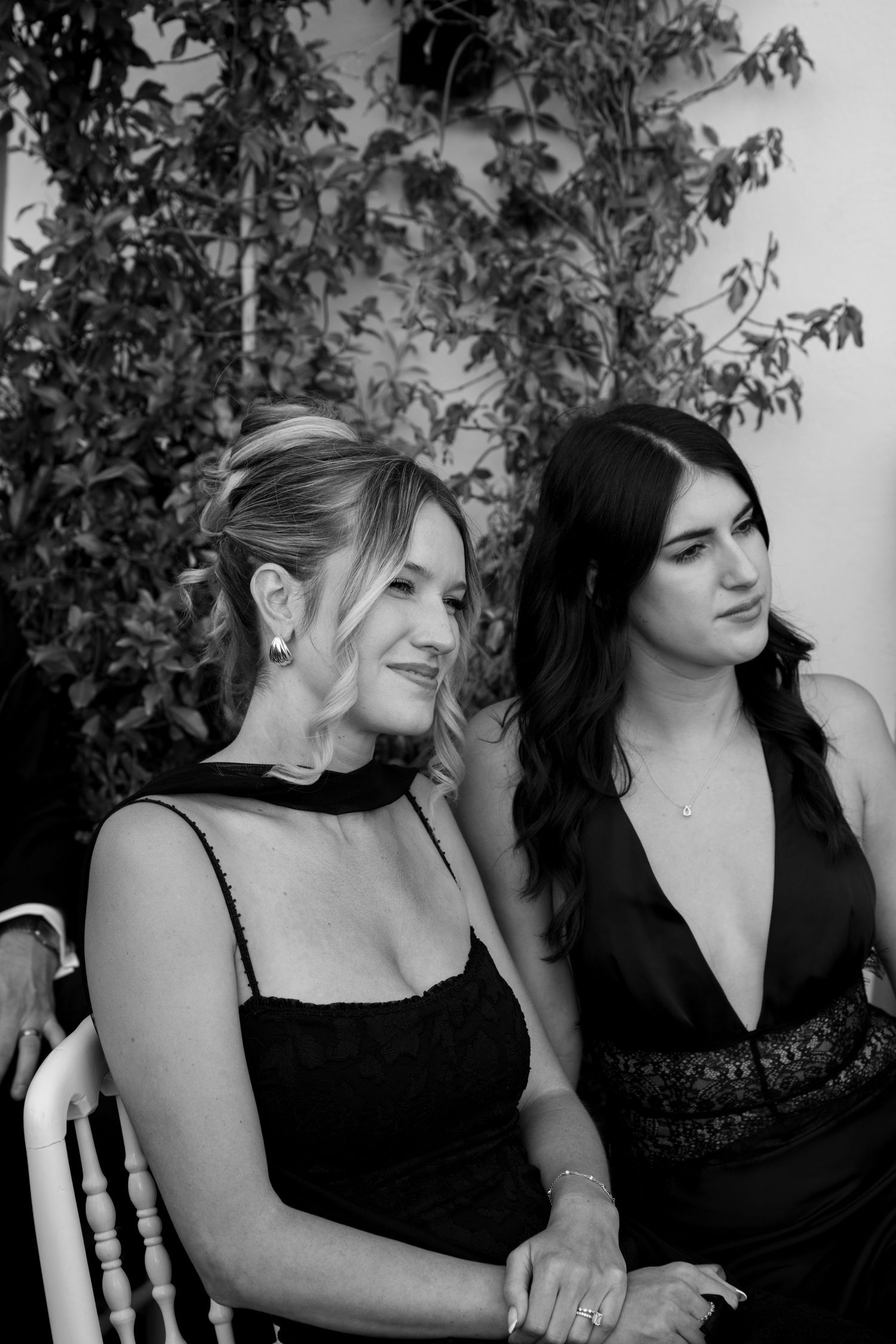 Two women in black dresses seated together at a wedding ceremony in black and white photo.