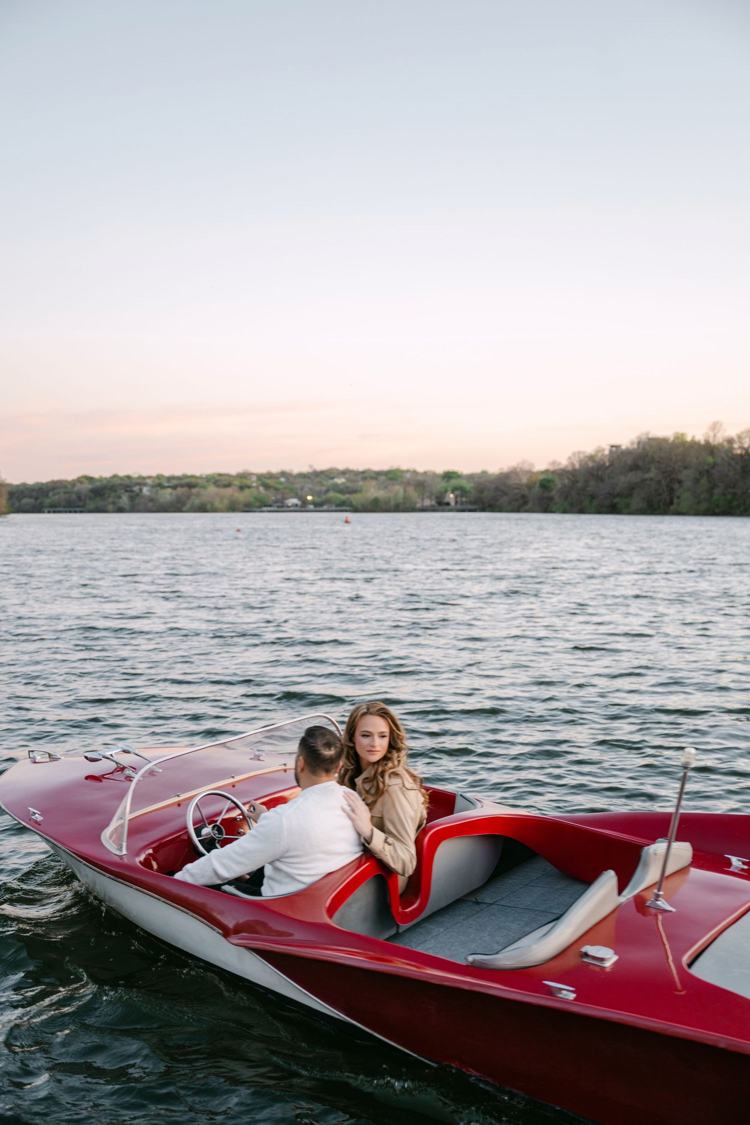 Couple sitting together in a classic red speedboat on a wide river at sunset.