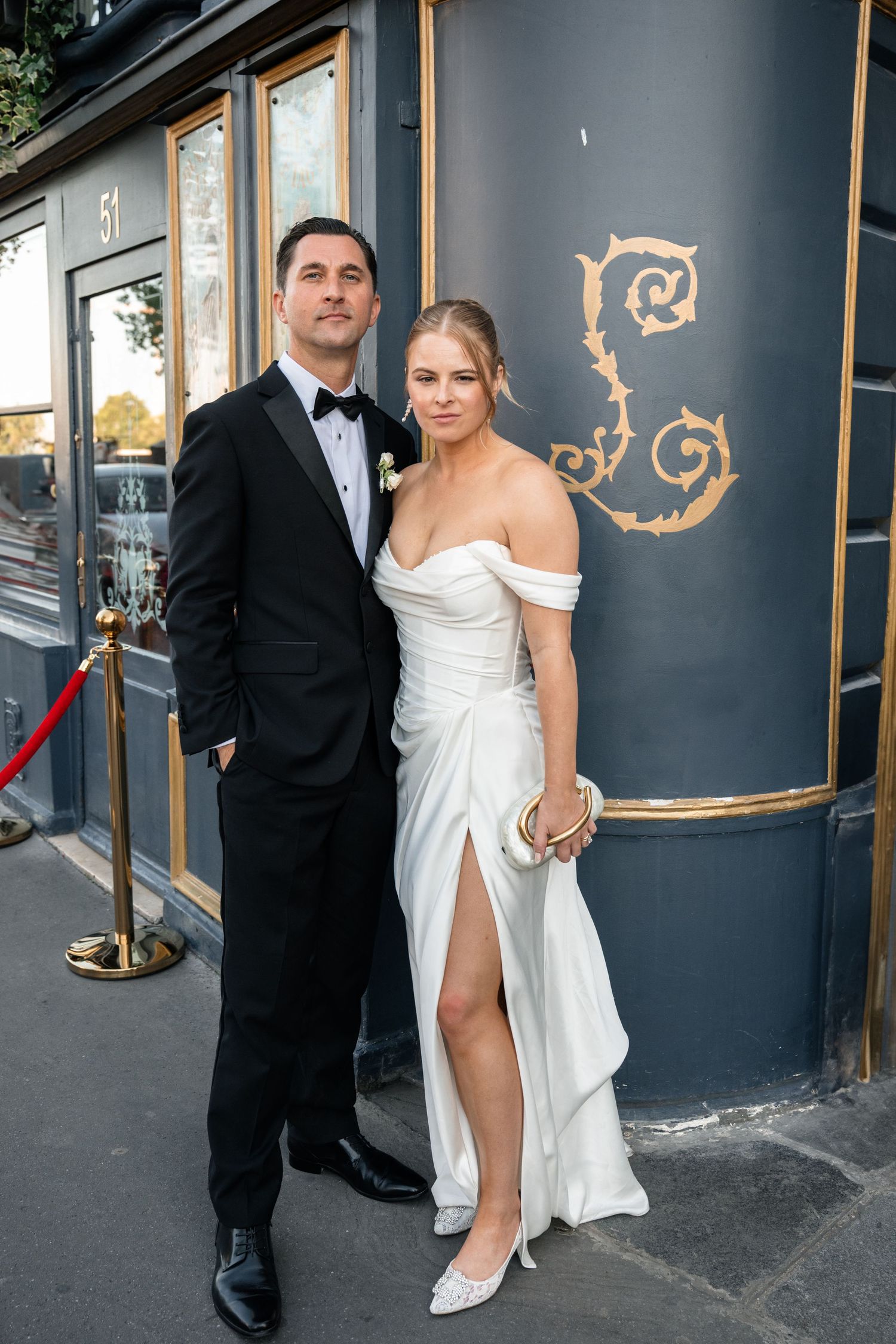 Wedding couple posing outside an elegant venue, bride in off-shoulder white gown.