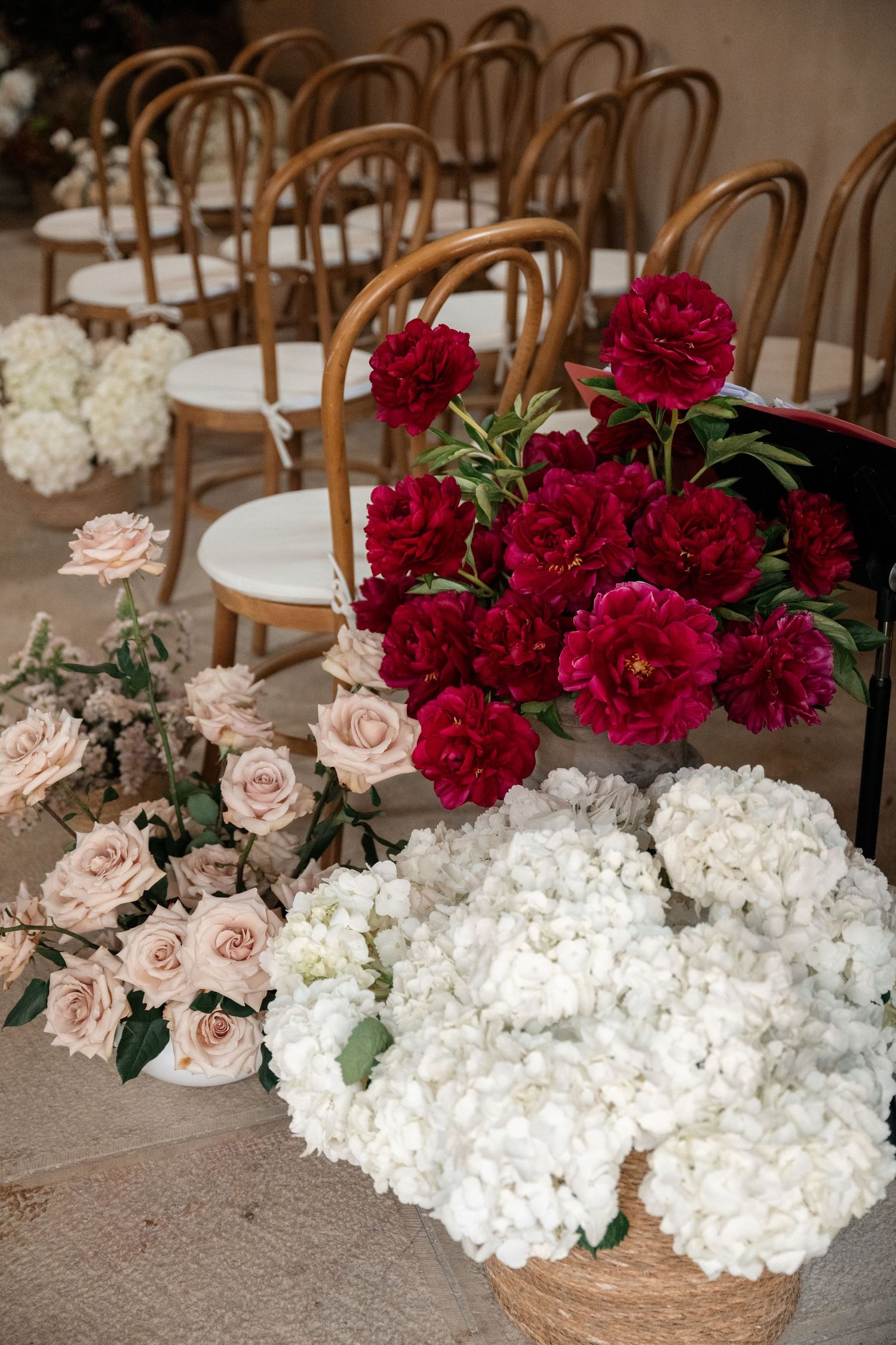 Elegant floral arrangements with deep red carnations, white hydrangeas, and blush roses alongside wooden chairs.