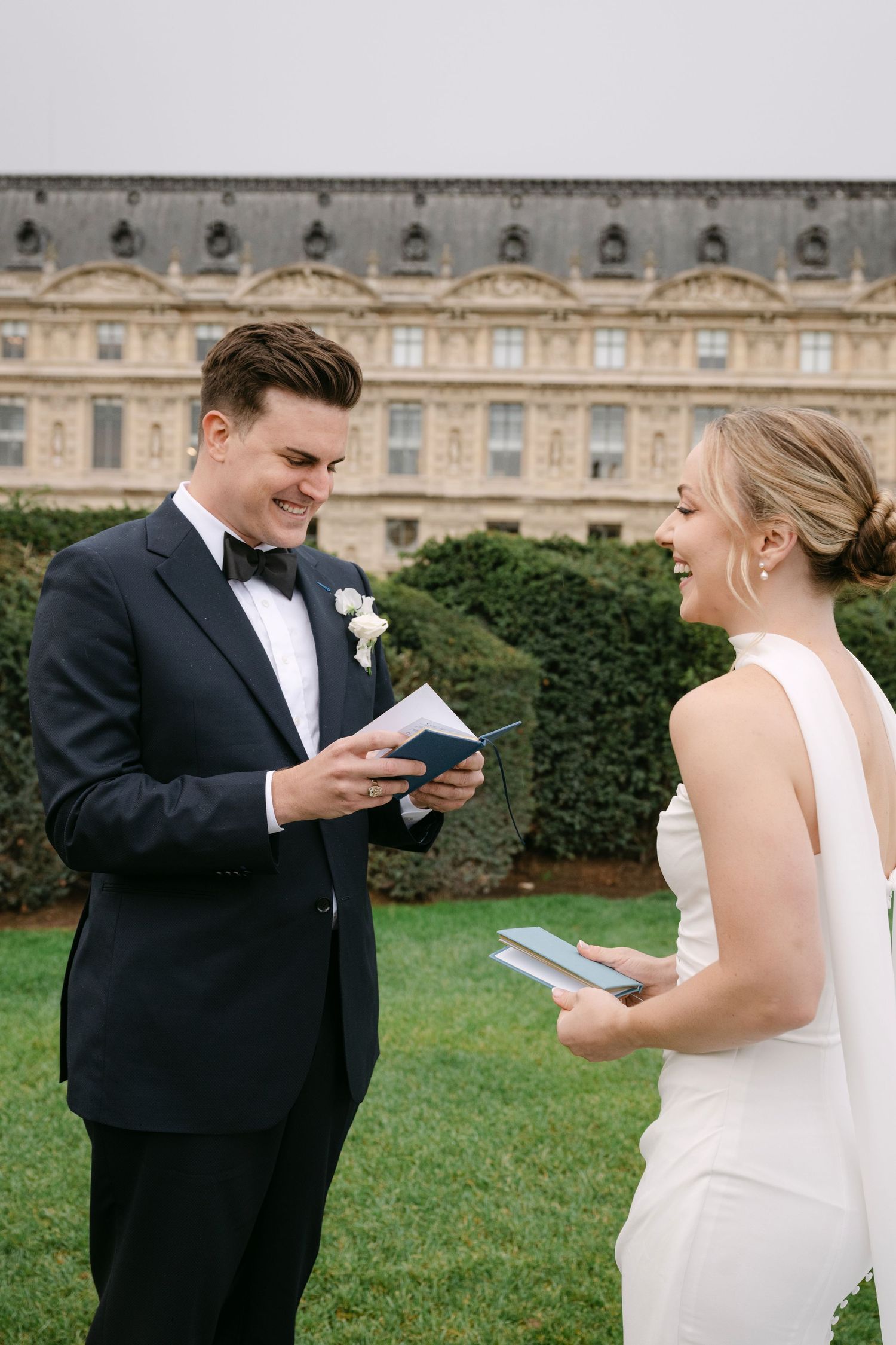 A couple shares an intimate moment while reading from small books in front of a grand historic building.