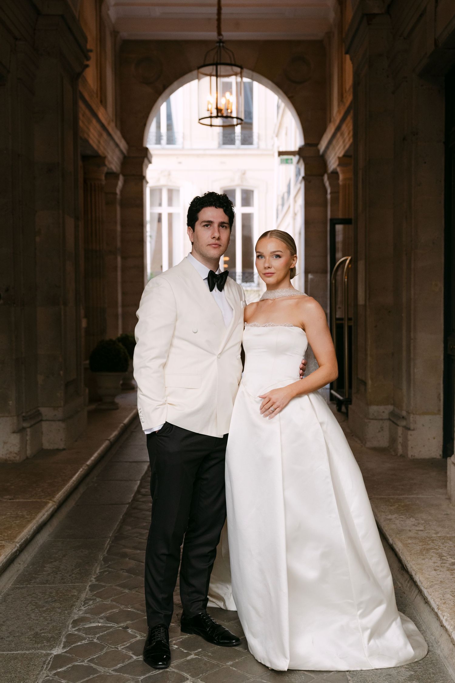 A wedding couple poses in a series of romantic shots under an elegant archway in a historic building.
