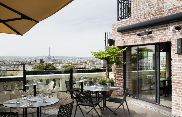Chic outdoor terrace dining area with panoramic Paris city views and Eiffel Tower in distance.