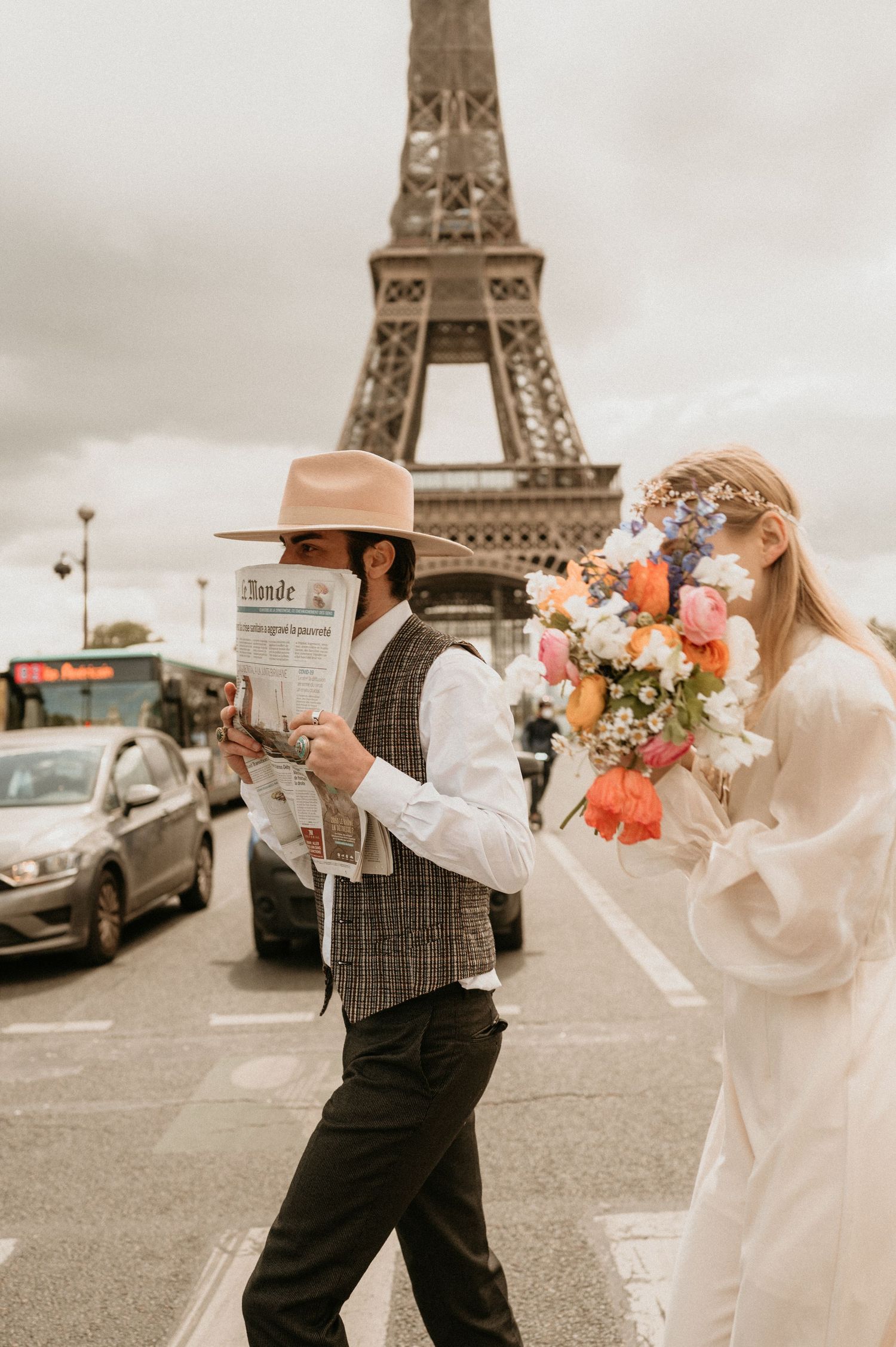 Stylish couple walking near Eiffel Tower with newspaper and spring bouquet.