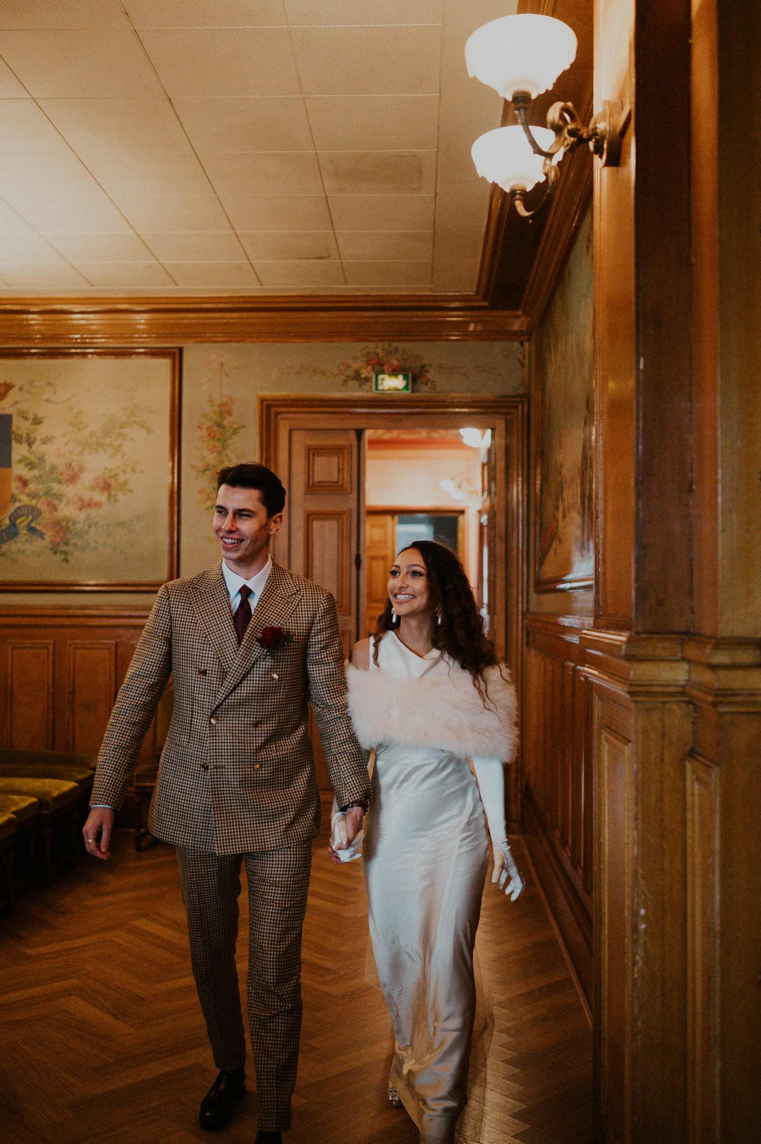 A couple walking hand in hand down a wood-paneled hallway with vintage decor.