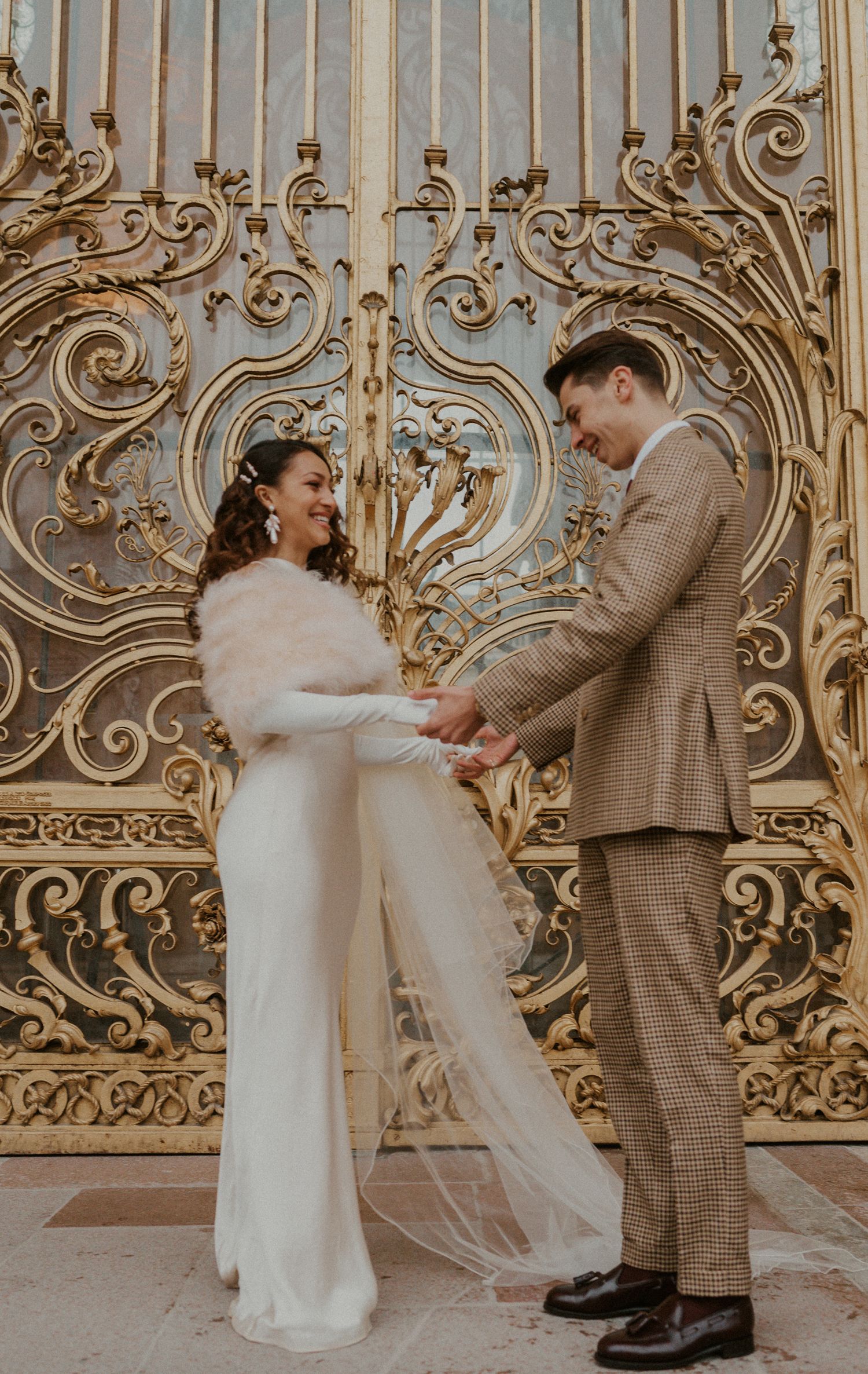 Couple shares intimate moment in front of decorative gold gates during wedding photoshoot.