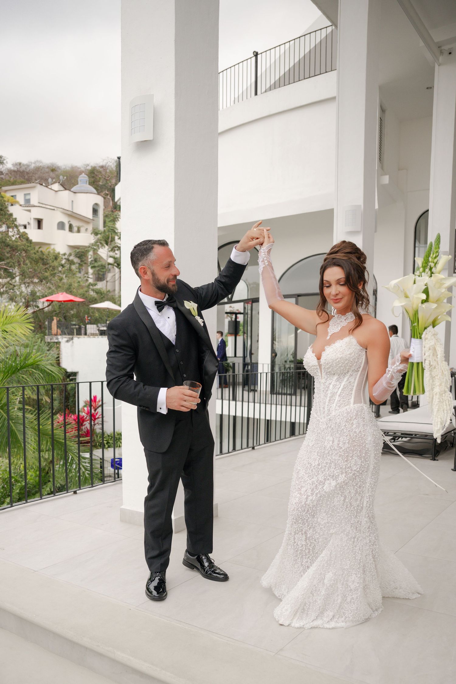Bride and groom share first dance on white venue balcony, groom spinning bride in lace wedding gown.