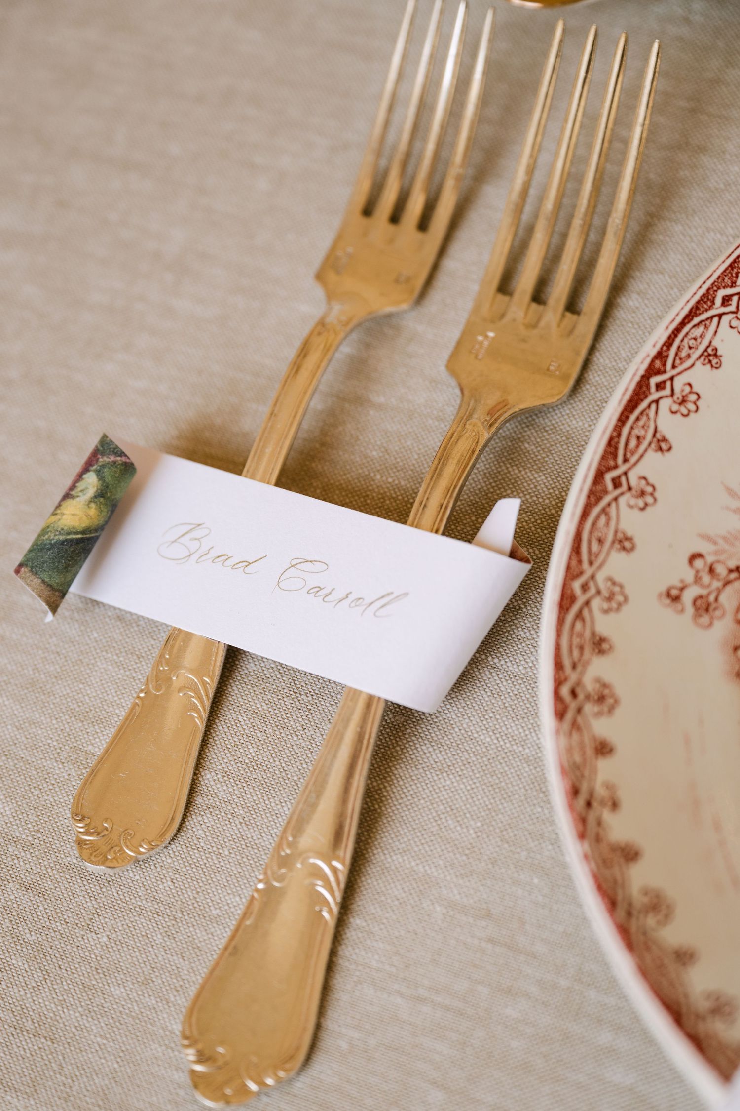 Gold cutlery and calligraphy place card reading Brad Carroll beside a red toile dinner plate.