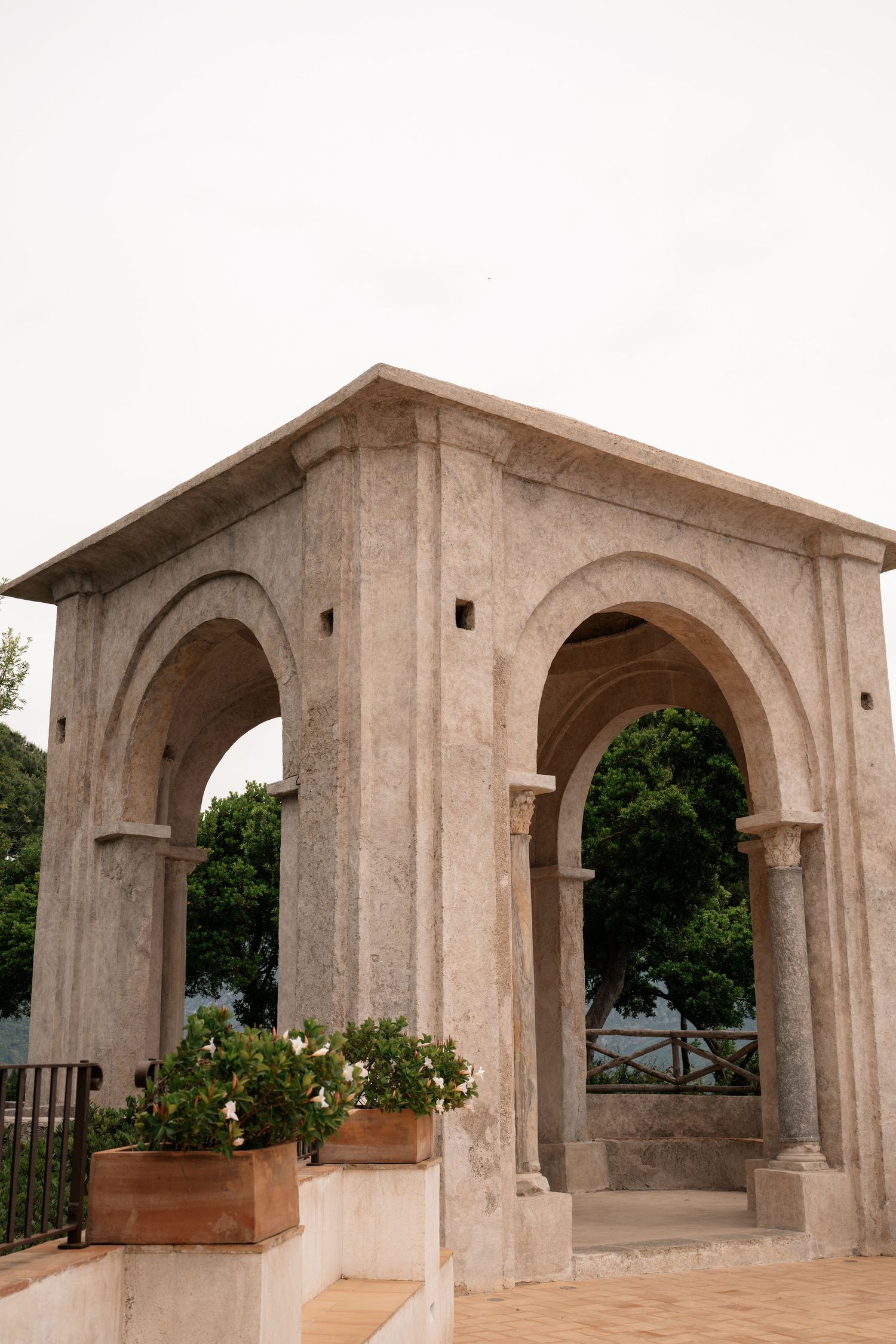 Classic marble double arch pavilion with potted white flowers at Italian villa garden terrace.