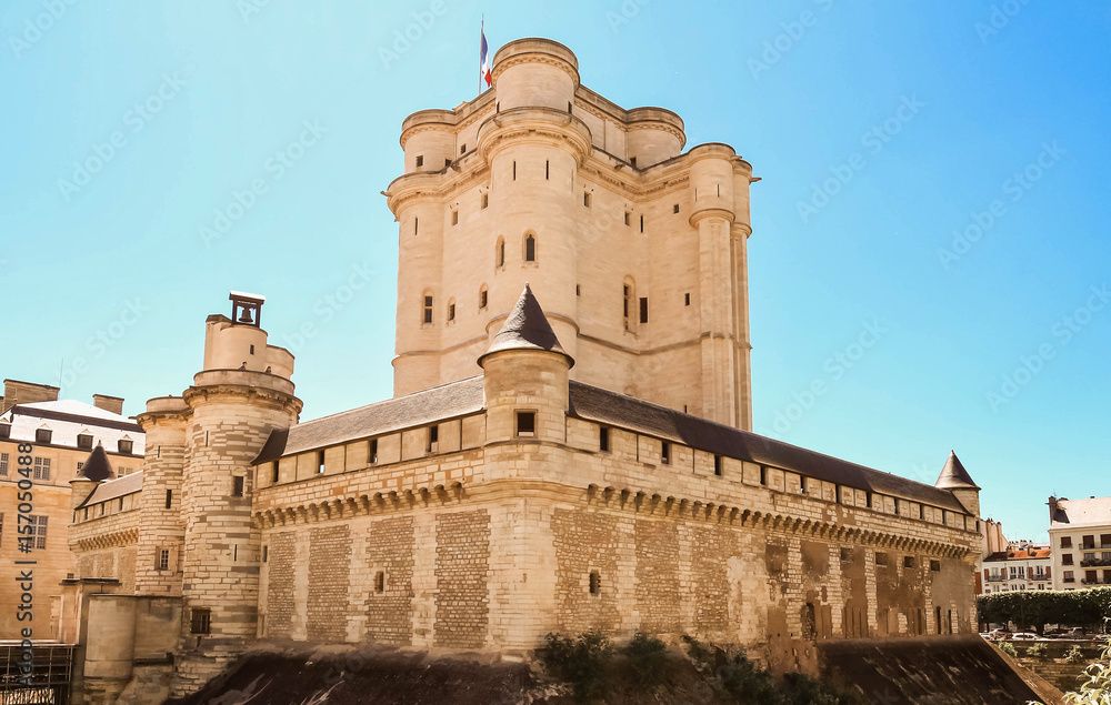 Historic stone fortress with circular towers and defensive walls under bright blue sky.
