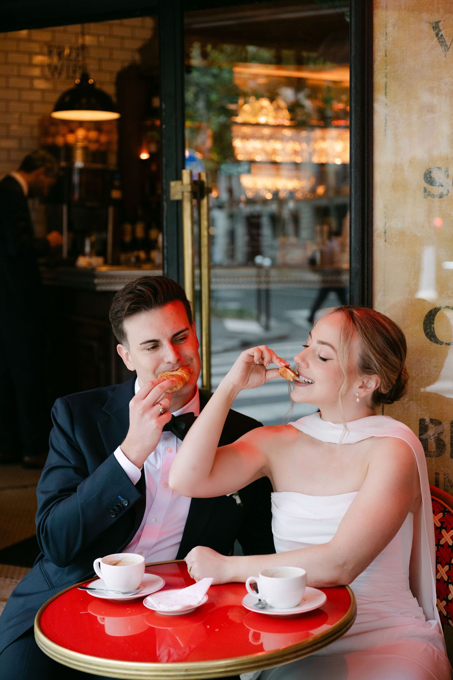 A couple shares playful moments while having coffee at a cafe with red tables.