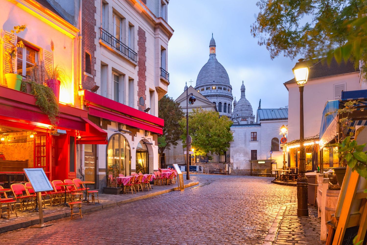 Charming cobblestone street in Montmartre with cafe terraces and view of Sacre-Coeur basilica.