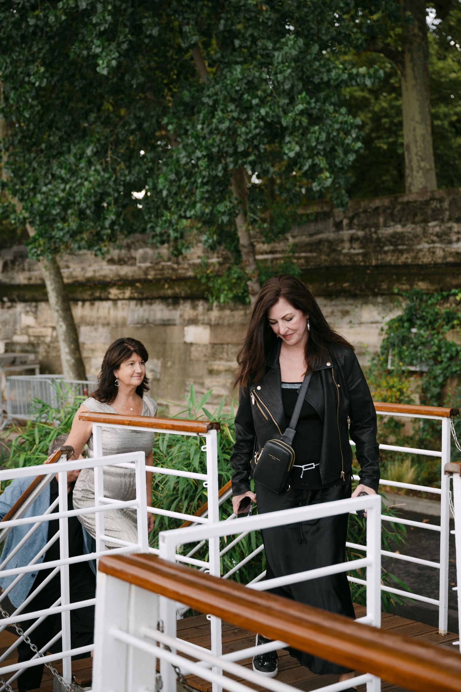 A couple sits together on a wooden bench with white railings in a garden setting with lush greenery.