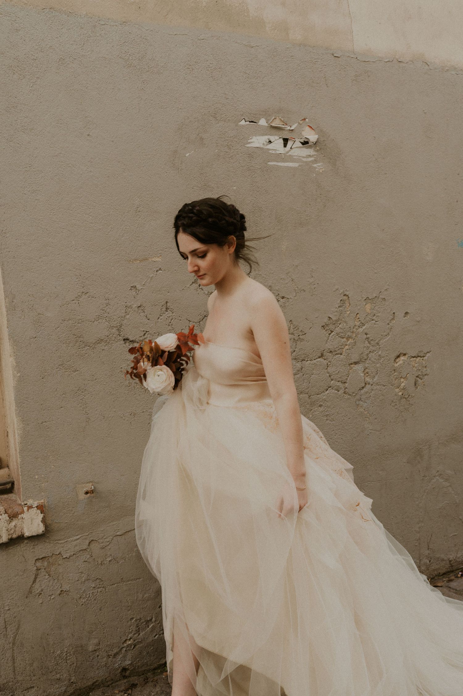 Ethereal wedding dress photograph with warm tones against weathered wall texture.