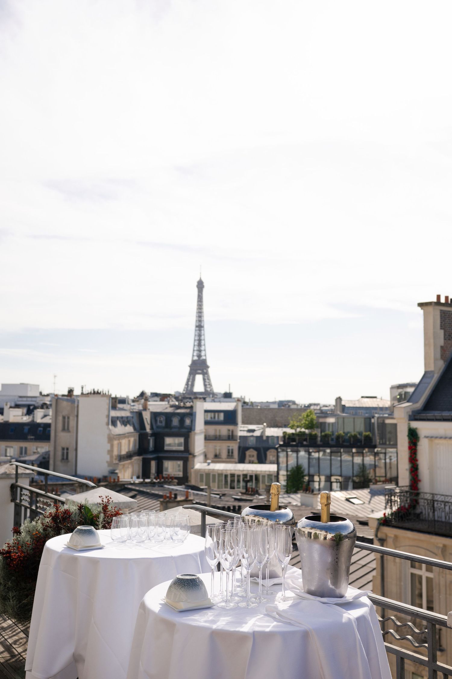 Elegant rooftop terrace in Paris with champagne glasses and Eiffel Tower view on a sunny day.