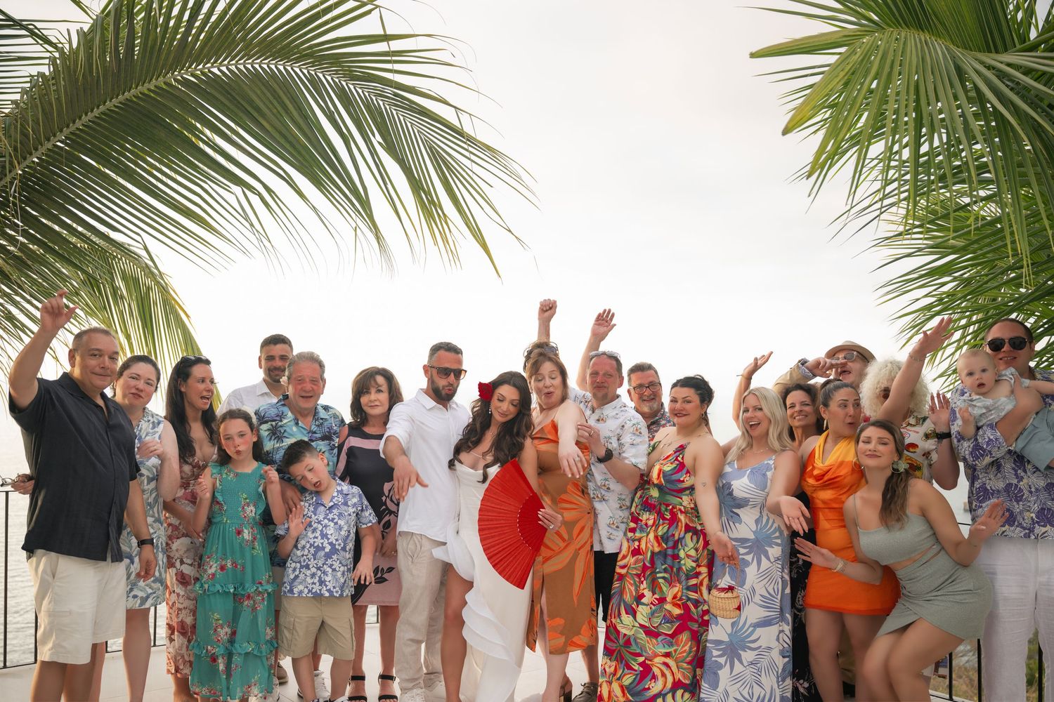 Large group of joyful guests celebrating a tropical beach wedding under palm trees.