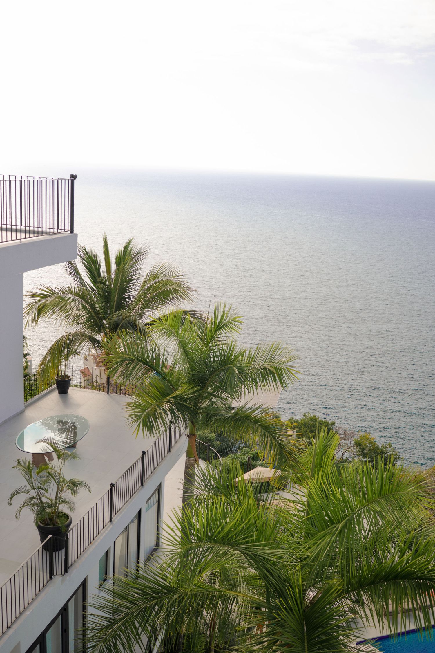 Luxury beachfront resort balconies with tropical palm trees overlooking calm ocean horizon on overcast day.
