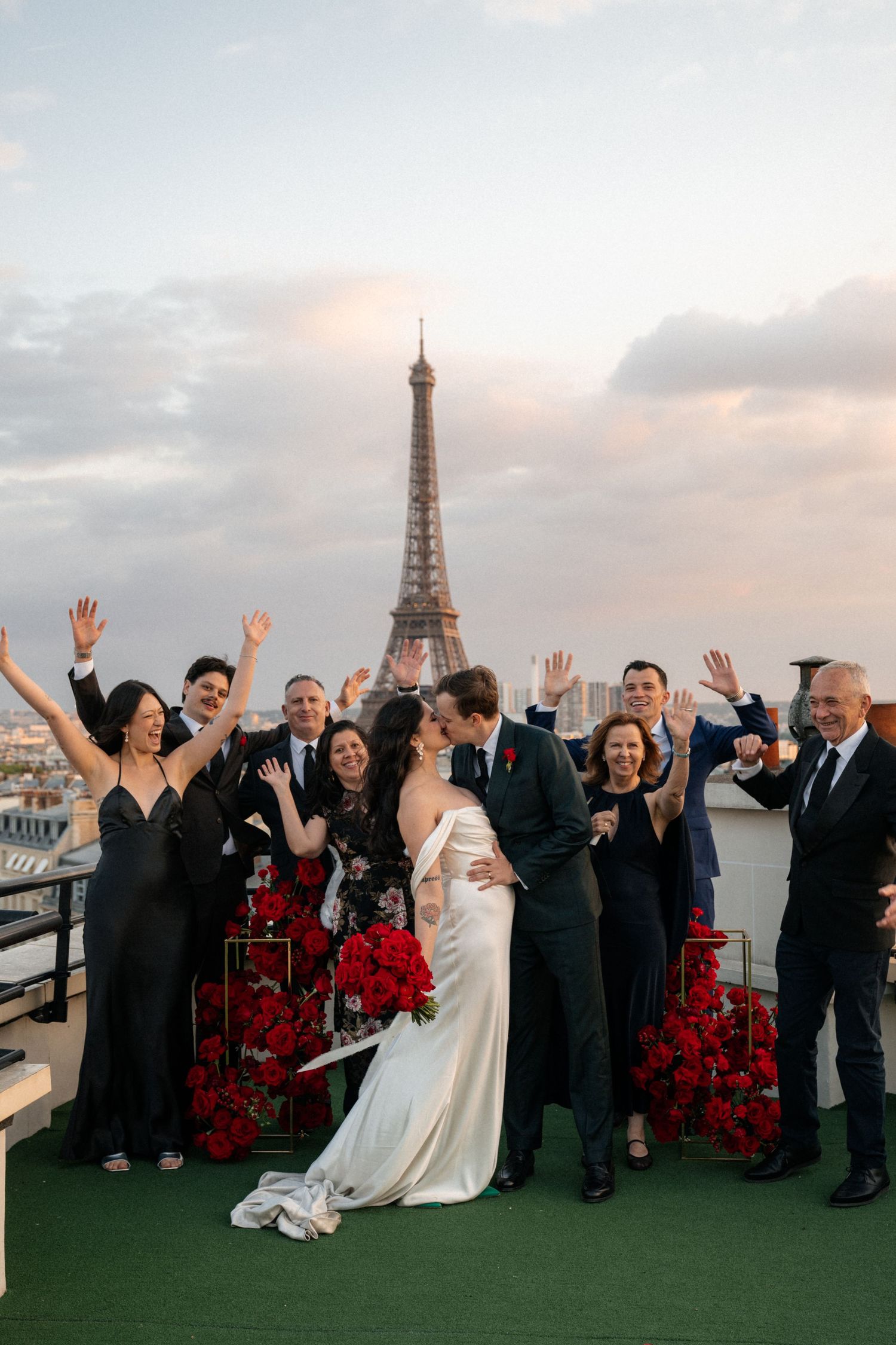 Wedding party celebrating on a rooftop with the Eiffel Tower visible in the background at sunset.