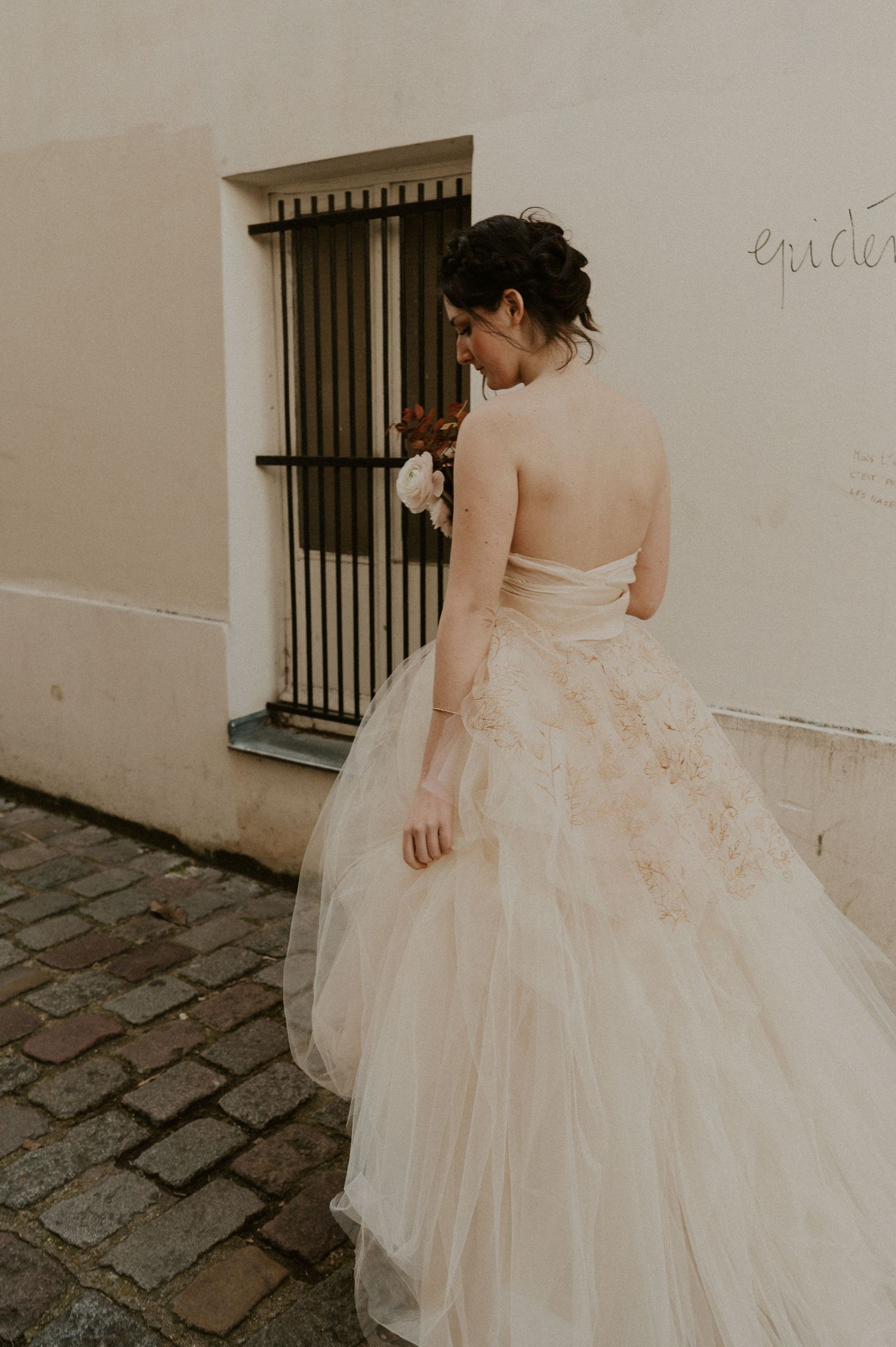 Back view of an elegant wedding gown with intricate embroidery details on a cobblestone street.