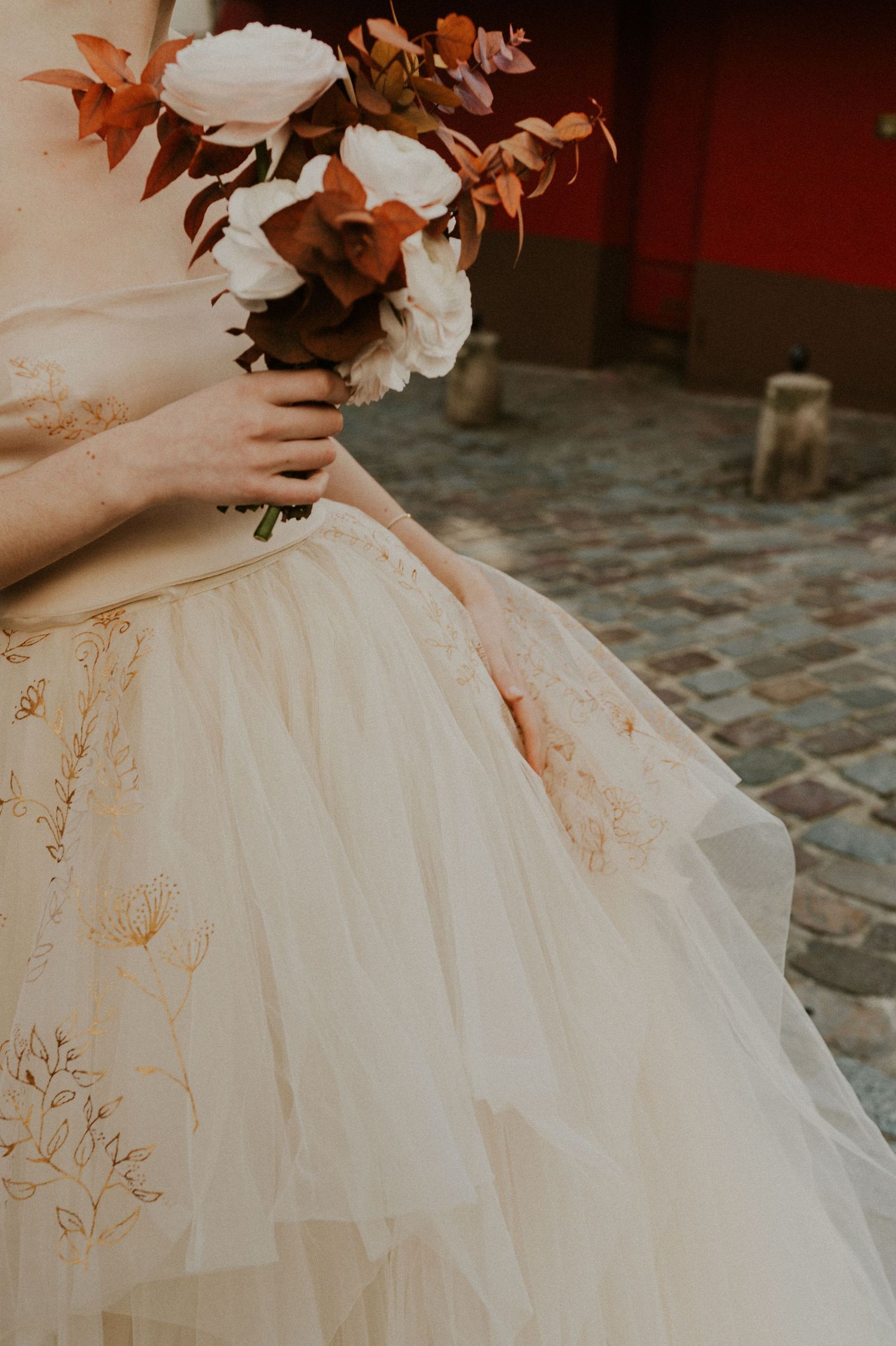 A detail shot of a champagne tulle wedding gown with autumn-colored floral bouquet.