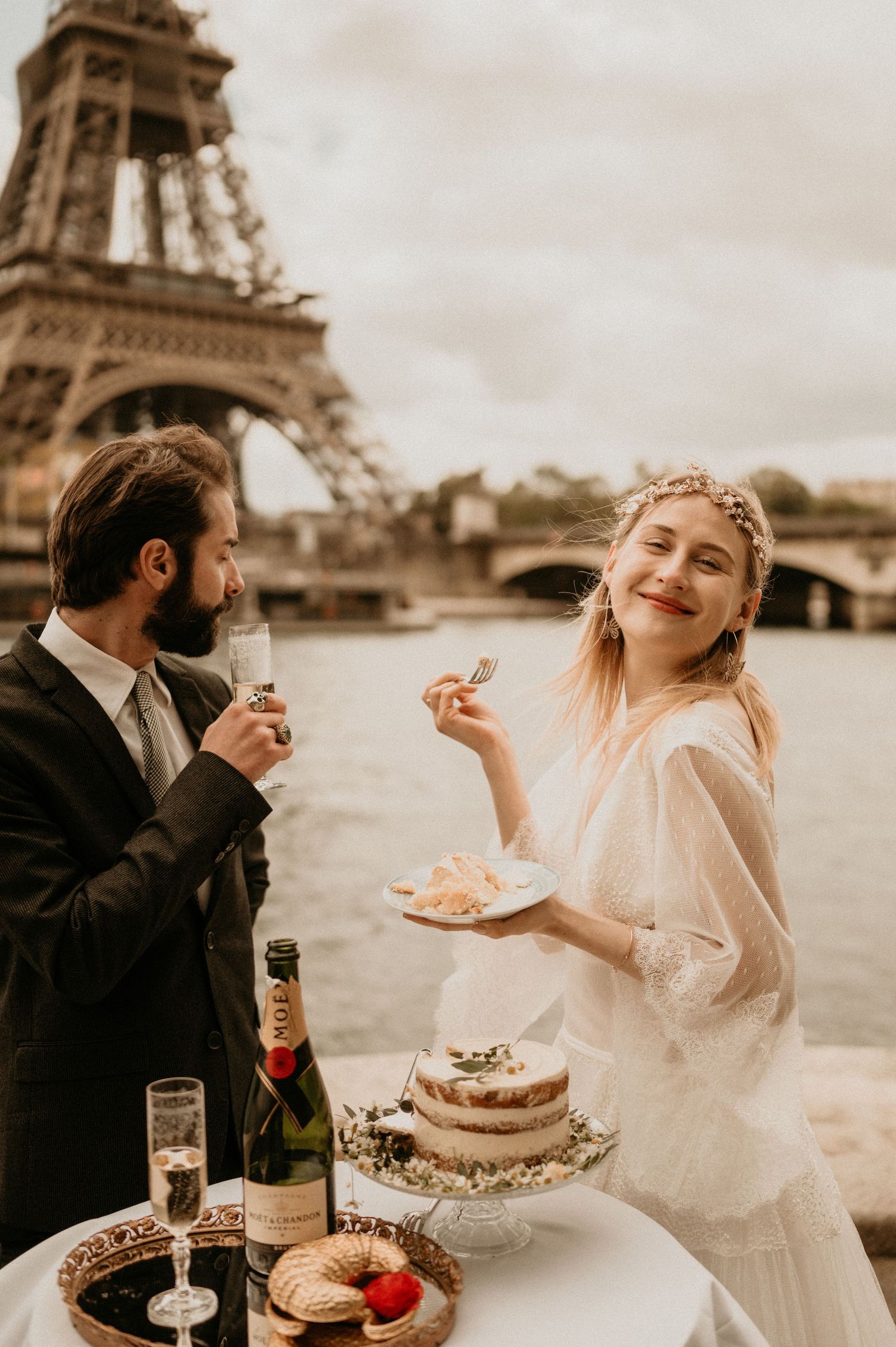 A joyful wedding moment with cake and champagne near the Seine River in Paris.