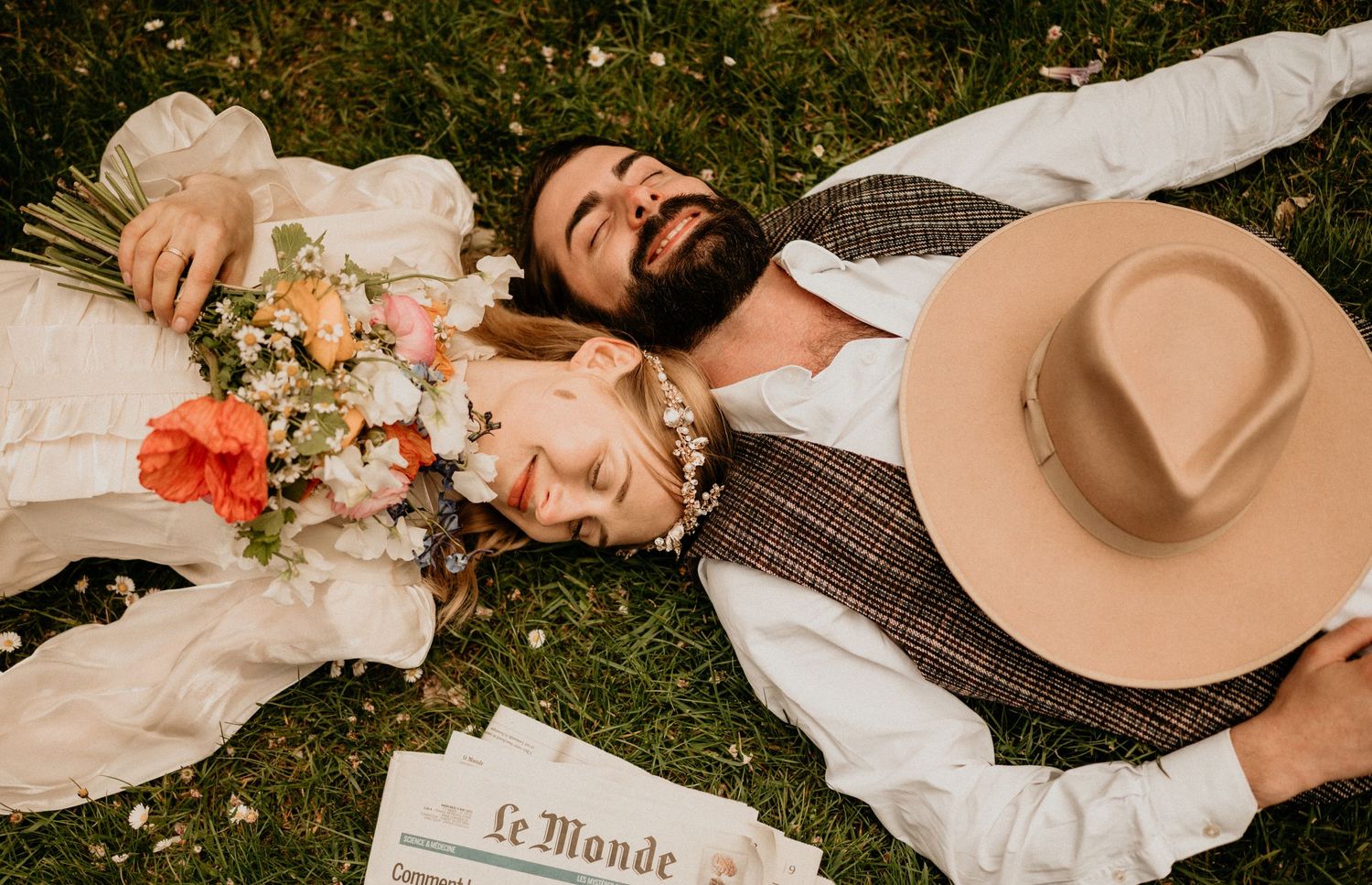 Couple relaxing on grass with bouquet and newspaper in warm afternoon light.