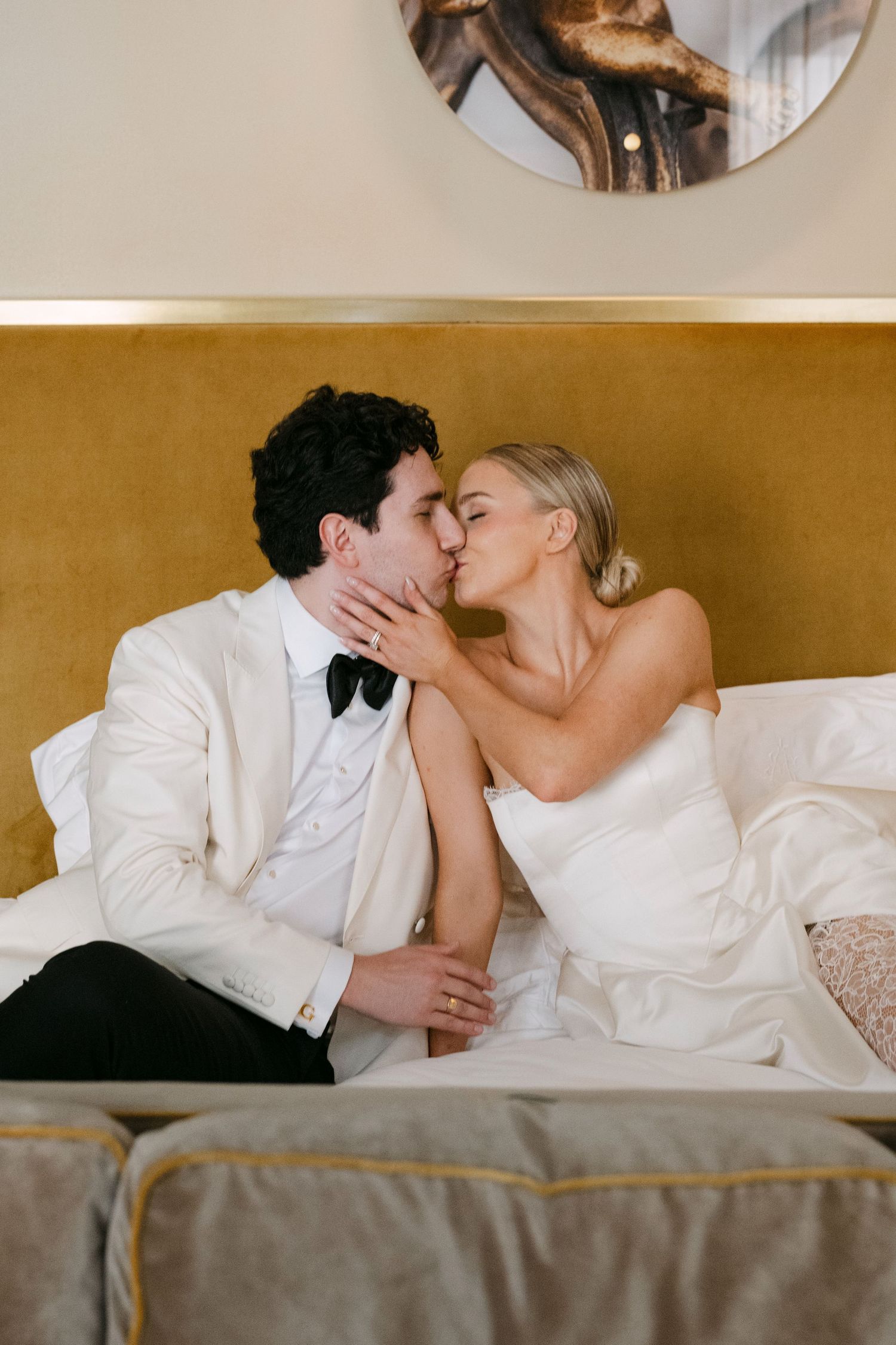 A couple in white attire sharing an intimate moment while lying on a bed.