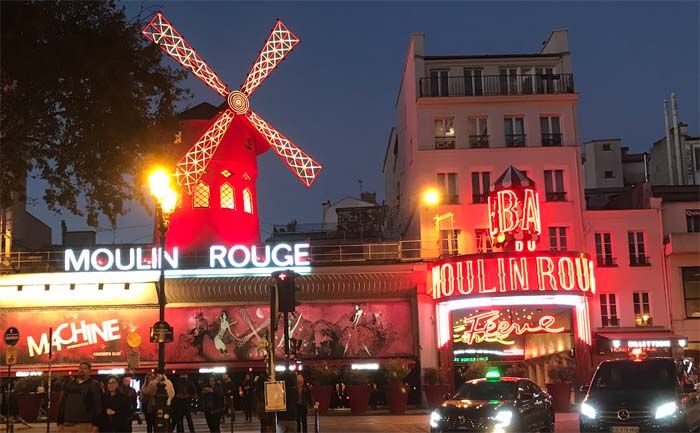 Iconic Moulin Rouge cabaret with red windmill illuminated at night in Paris.