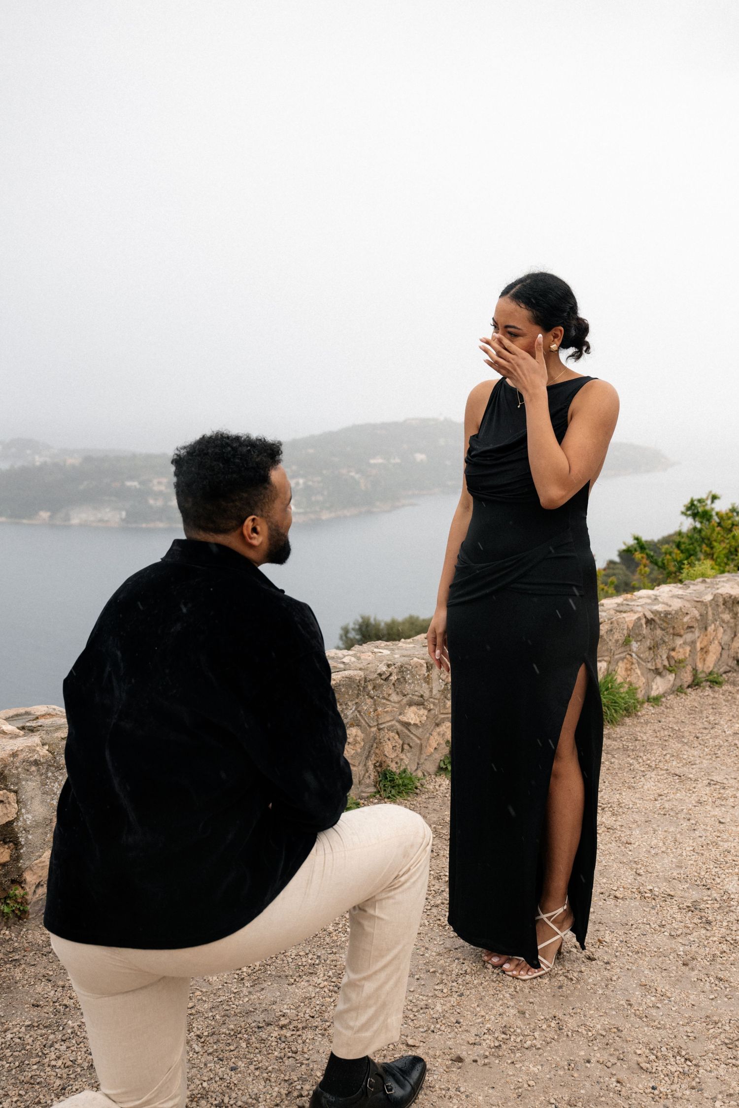 A romantic black and white embrace of a couple at a scenic overlook with cityscape and water views in the background.