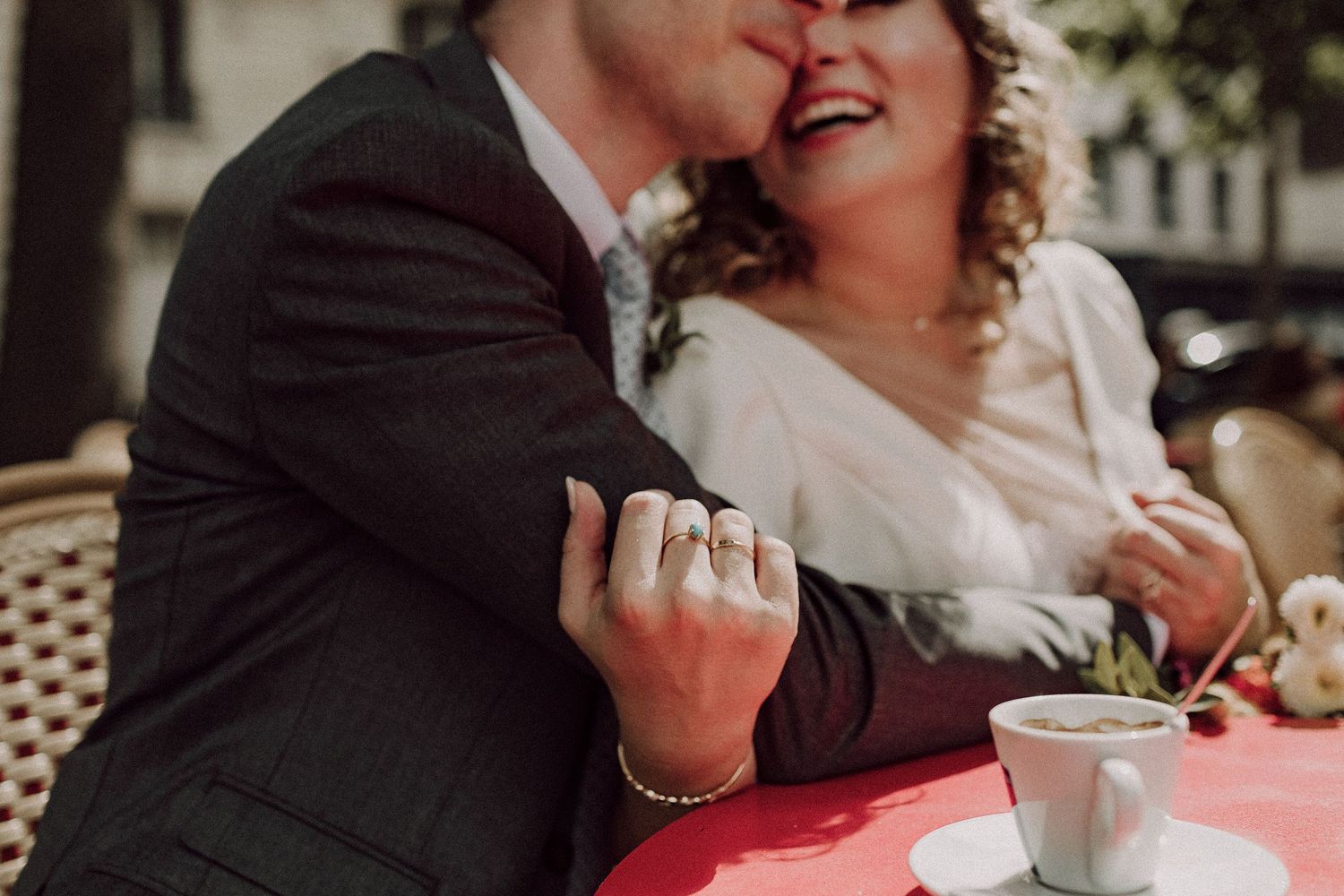 Close-up of newlyweds sharing a joyful moment at a red cafe table.