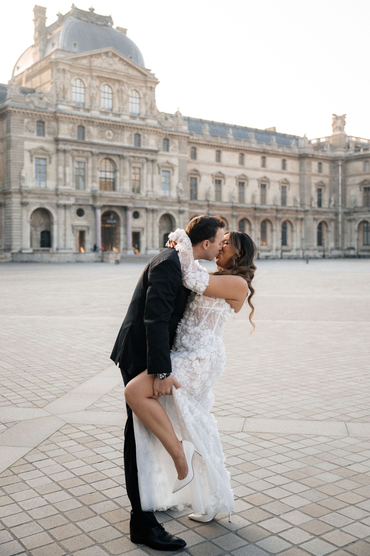 Newlyweds share an intimate moment while seated on a teal bed in a luxurious Parisian room.