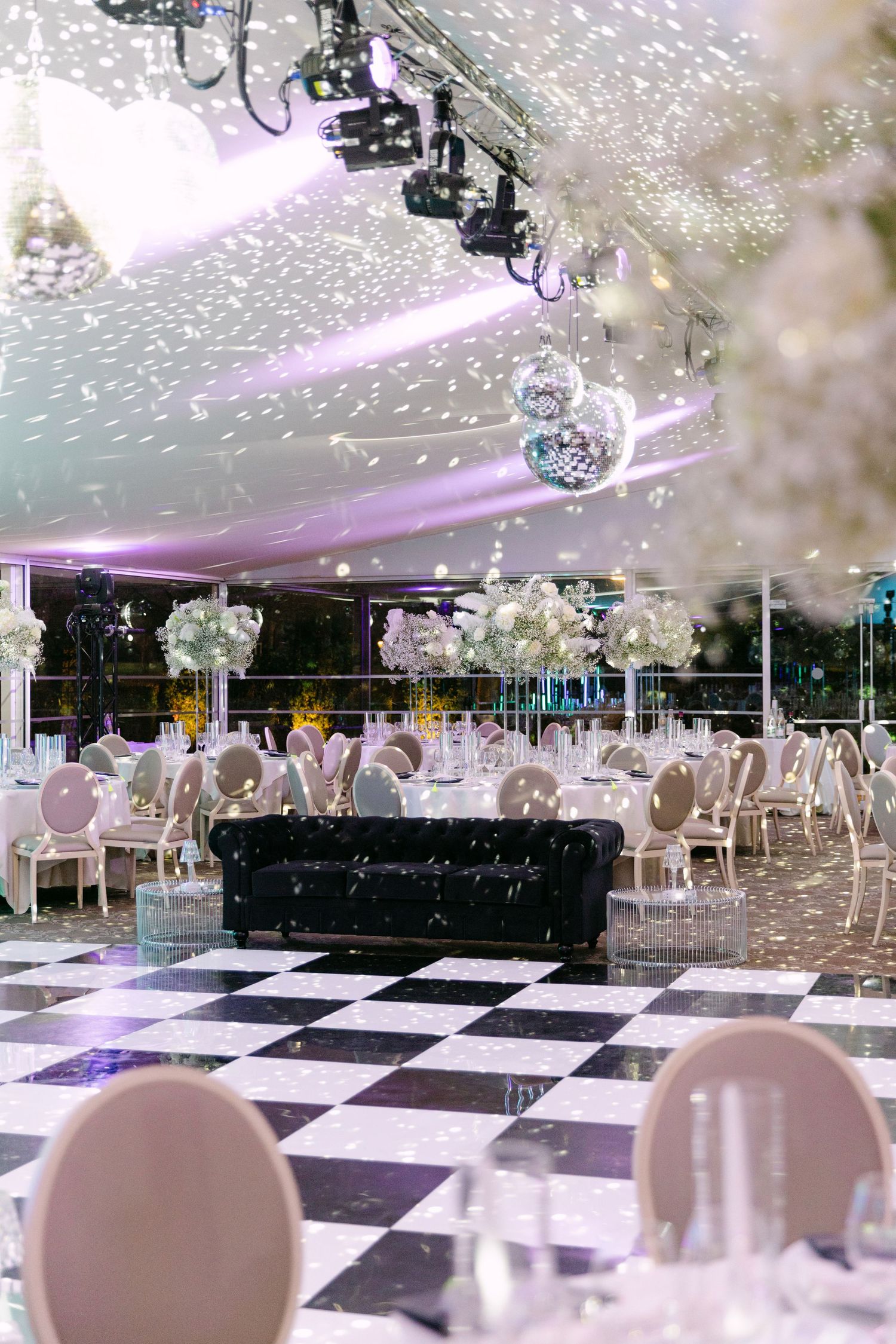 Elegant wedding reception venue with black and white checkered dance floor, disco balls, and floral centerpieces.