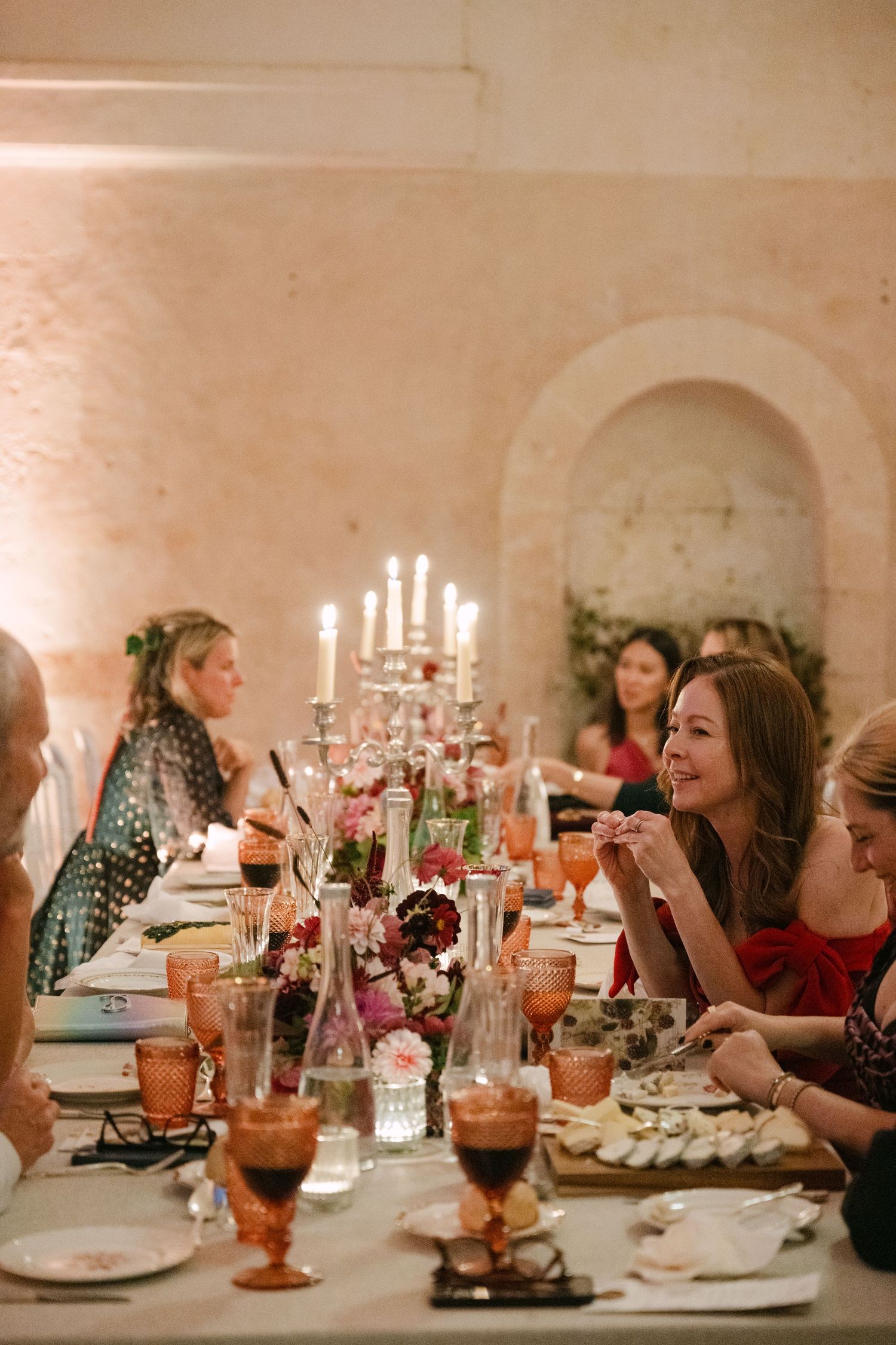 Wedding guests dining at candlelit table with floral arrangements and amber glassware in stone venue.