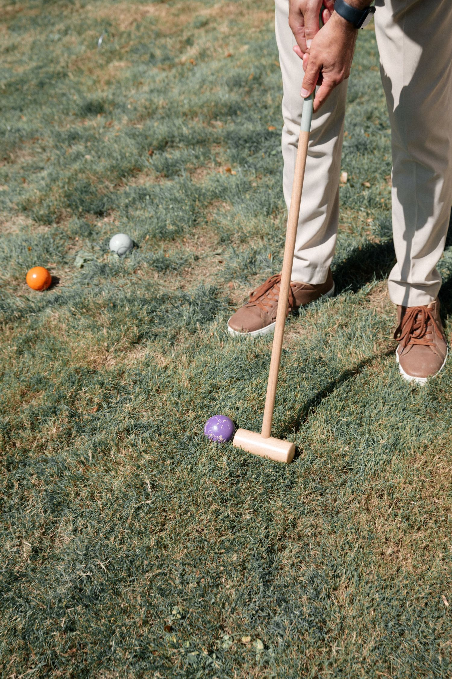 Person playing croquet on grass lawn with colorful balls during an outdoor garden party event.