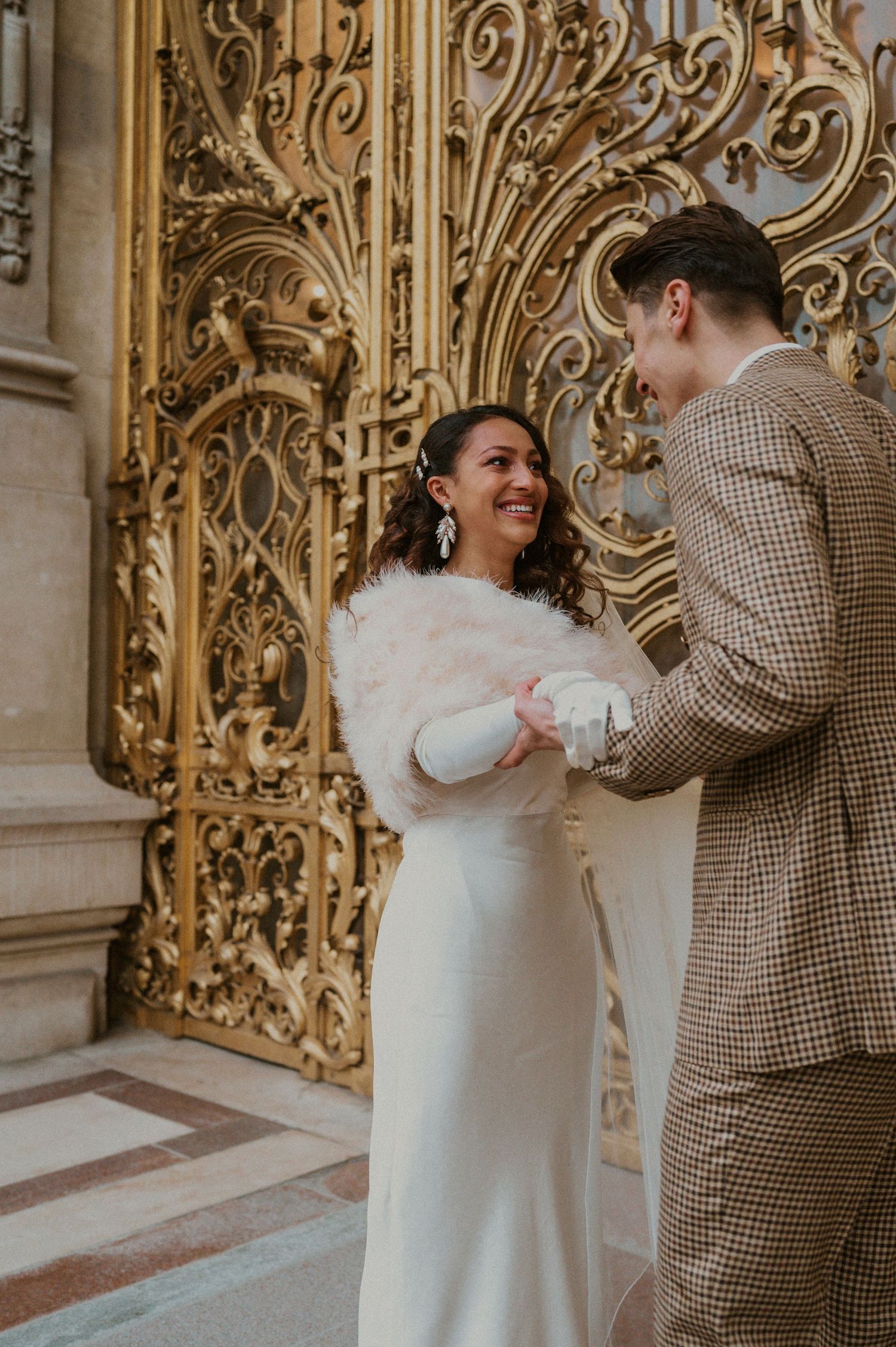 Happy couple embracing in front of ornate golden gates during their wedding celebration.