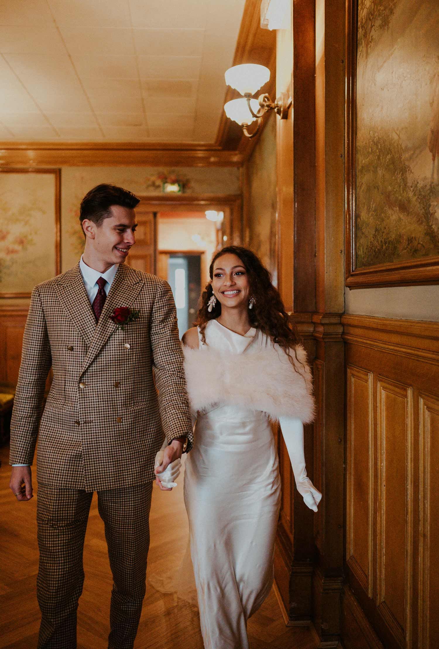 A happy couple walking through an elegant vintage hallway with wood paneling and classic lighting.